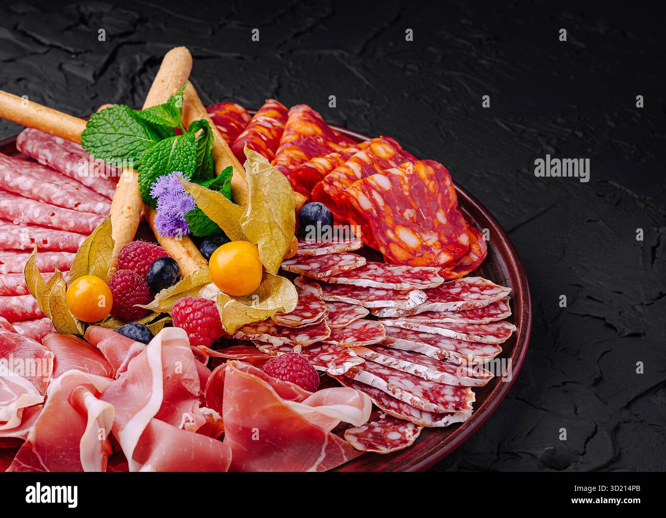 Viandes et fruits salés disposés magnifiquement sur un plateau sombre pour une présentation gourmande Banque D'Images