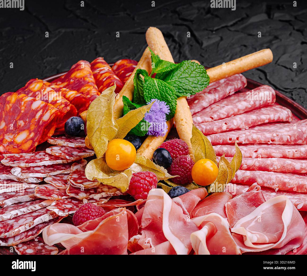 Viandes et fruits salés disposés magnifiquement sur un plateau sombre pour une présentation gourmande Banque D'Images