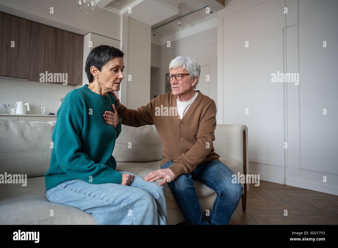 Femme choquée réagit aux nouvelles déchirantes, attrape la poitrine dans une crise cardiaque anxieuse tandis que l'homme inquiet tient près sur le canapé de la maison. Surcharge émotionnelle, chagrin Banque D'Images