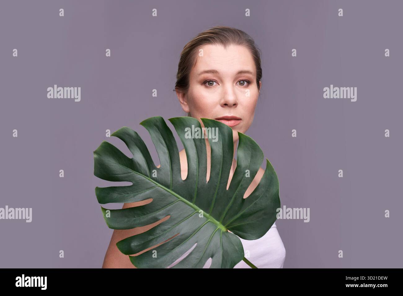 Femelle adulte caucasienne posant avec une feuille de monstera sur fond gris Banque D'Images