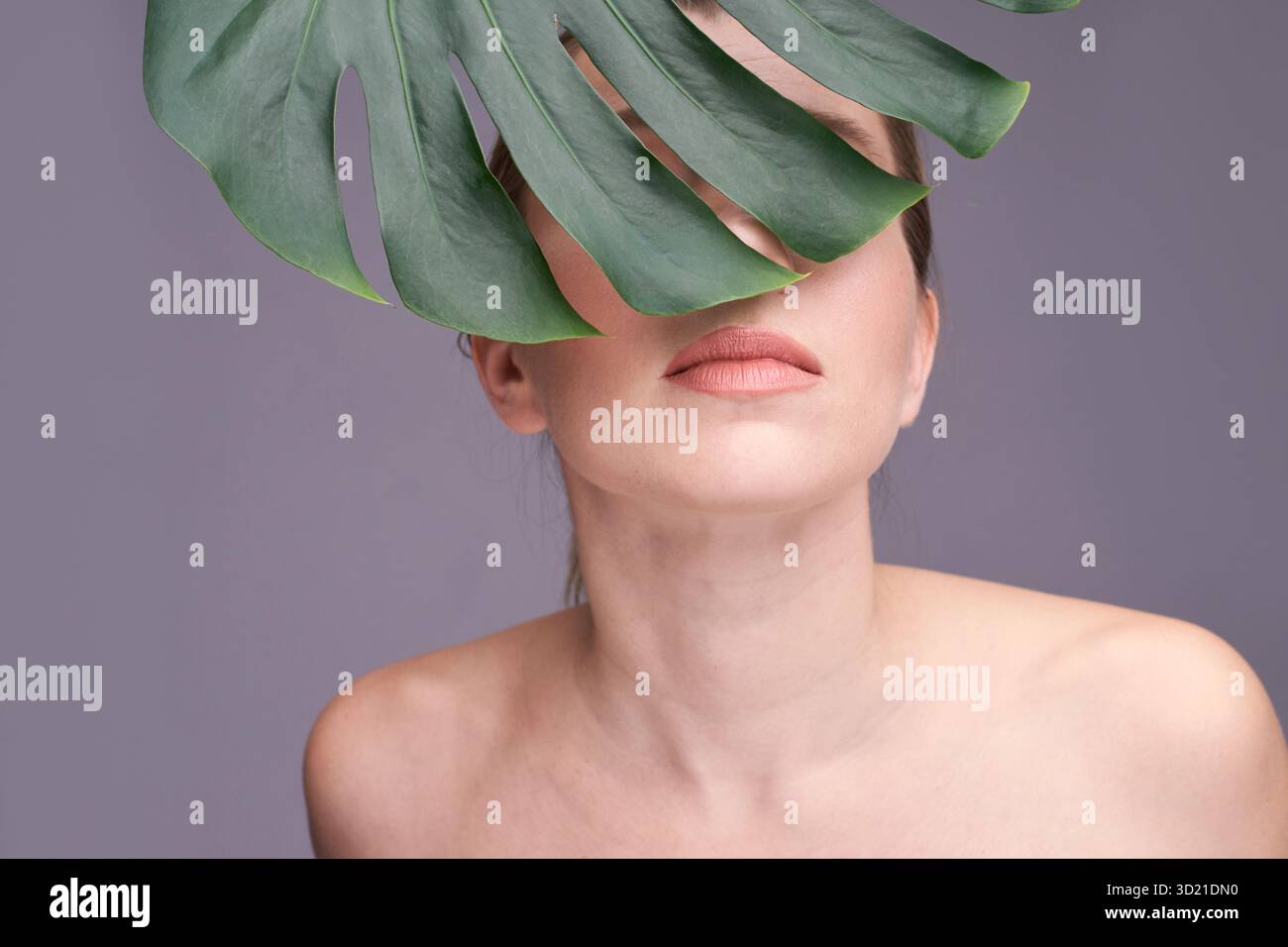 Jeune femelle caucasienne partiellement couverte par la feuille de monstera avec neutre Banque D'Images