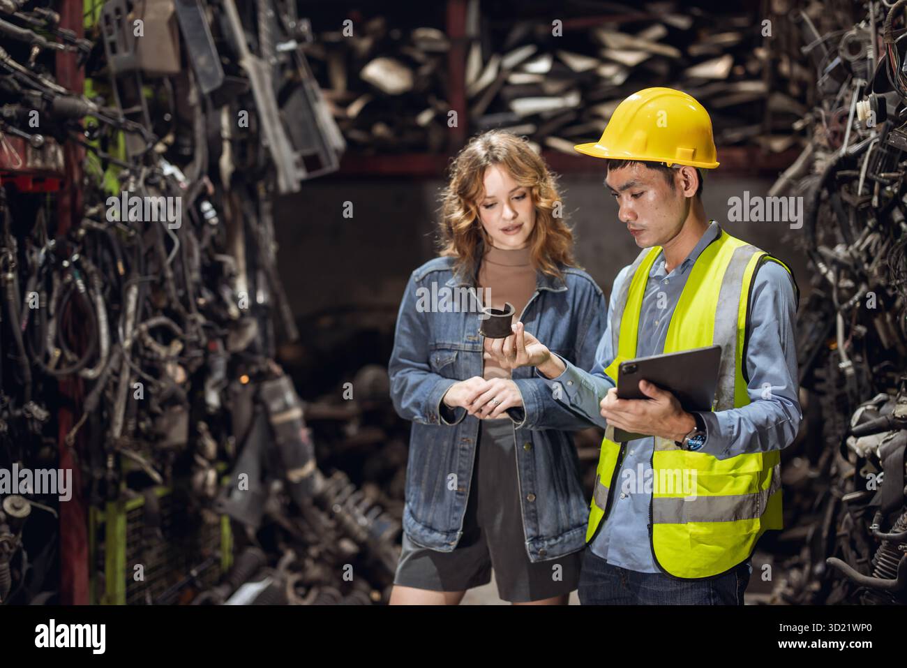 Technicien ouvrier masculin travaillant dans l'entrepôt d'atelier de vieil atelier de pièces de voiture de cour de ferraille de garage avec les femmes client trouvant la pièce de rechange pour la voiture Banque D'Images