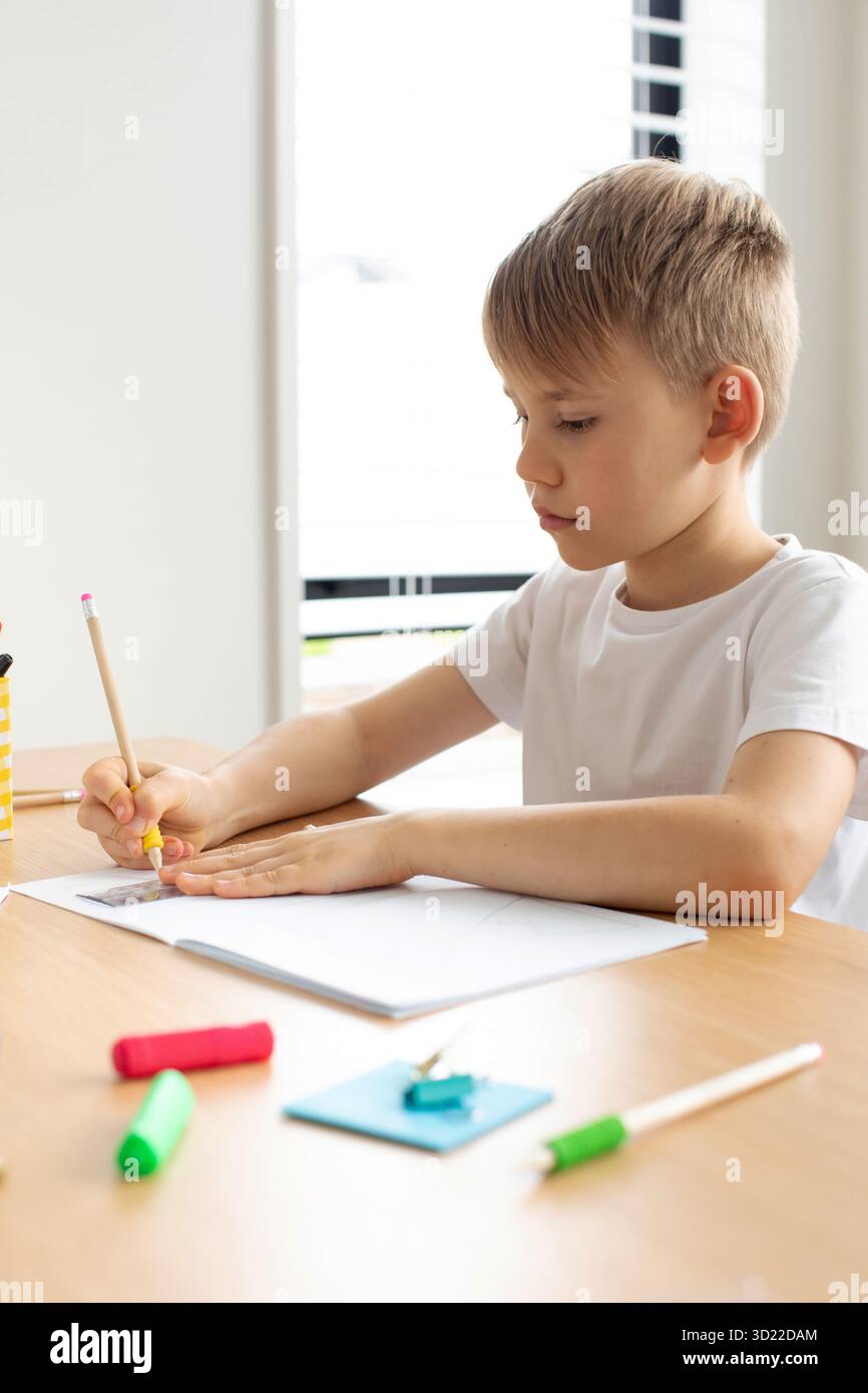 Un joli garçon fait un dessin avec une règle et un crayon. Leçons à la maison. Géométrie et dessin. Banque D'Images
