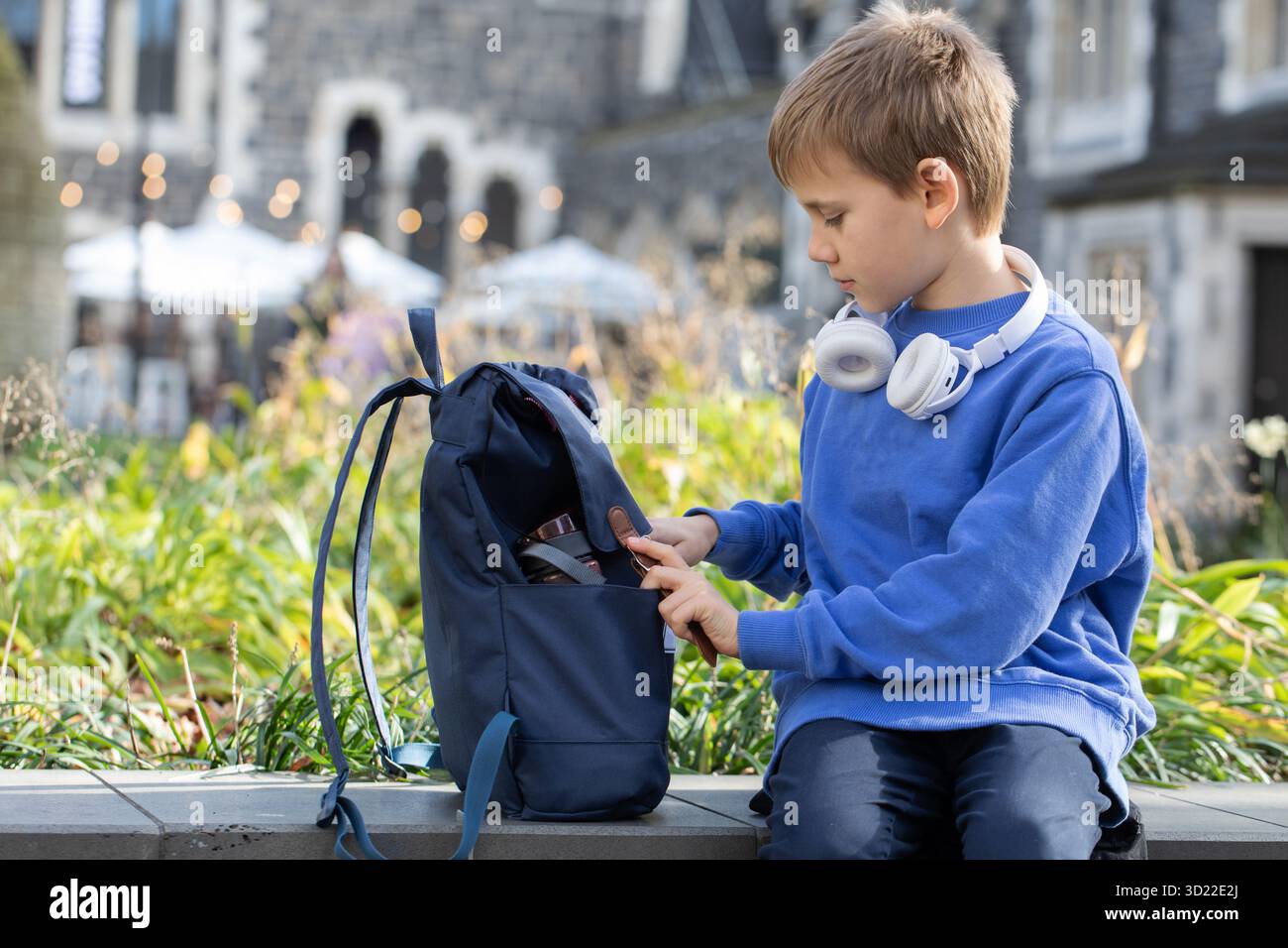 Un élève garçon souriant avec des écouteurs sans fil ouvre le cartable Banque D'Images