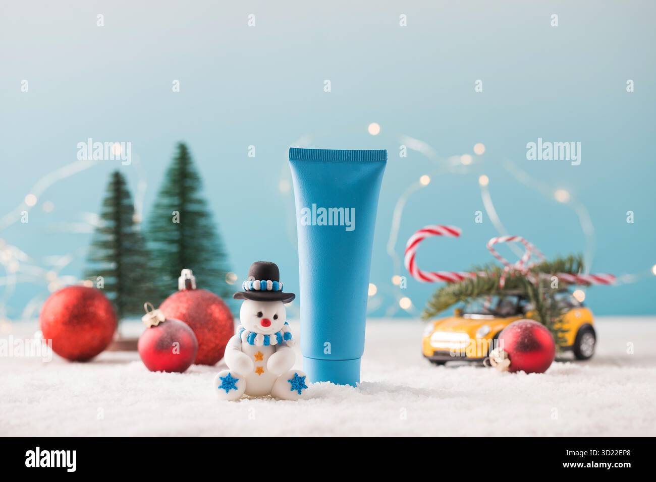 Maquette d'un tube bleu avec un produit cosmétique avec un bonhomme de neige sur un fond de Noël avec de la neige qui tombe. Banque D'Images