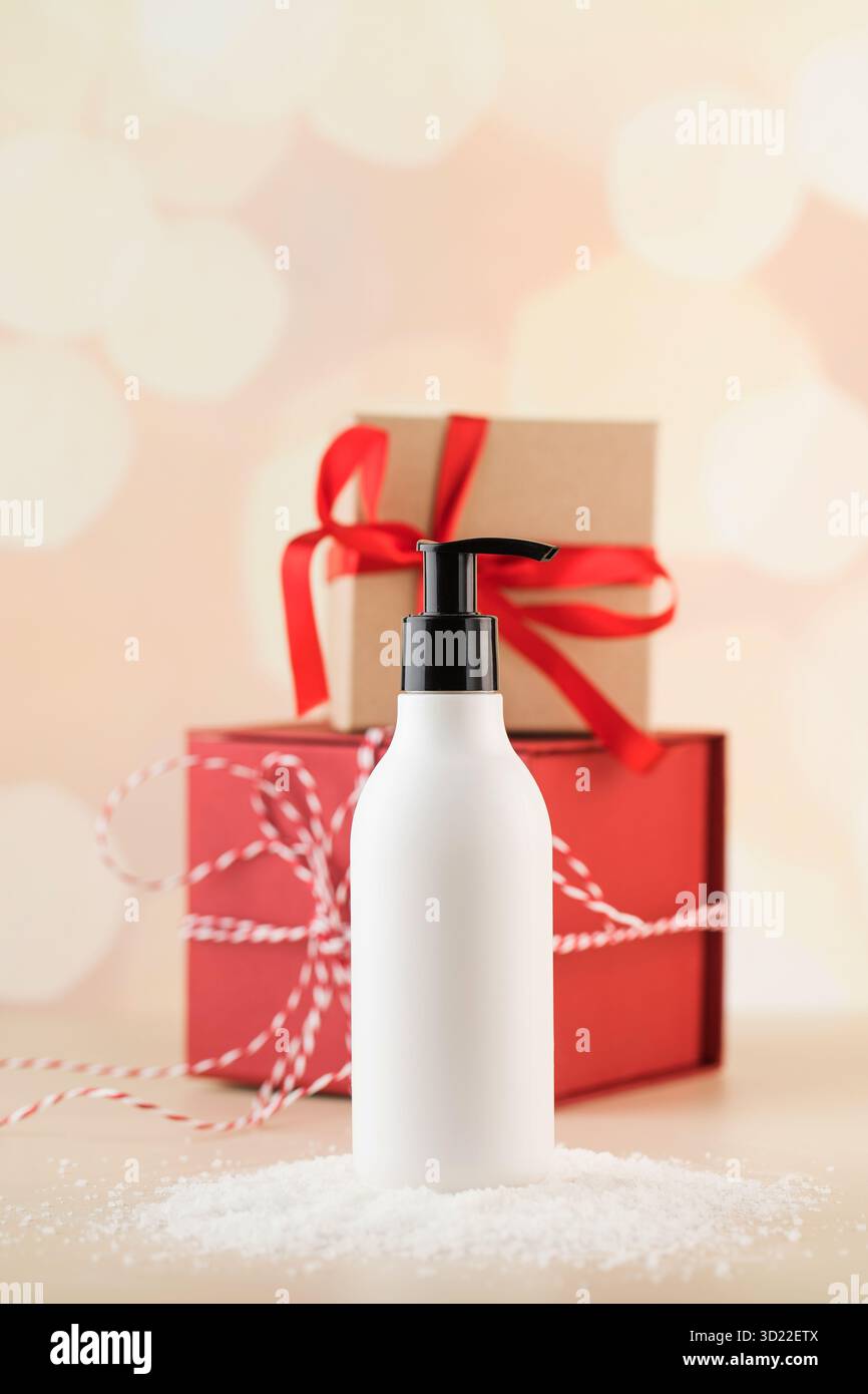 Maquette d'un distributeur blanc avec un produit cosmétique sur la neige sur fond de cadeaux de Noël. Banque D'Images