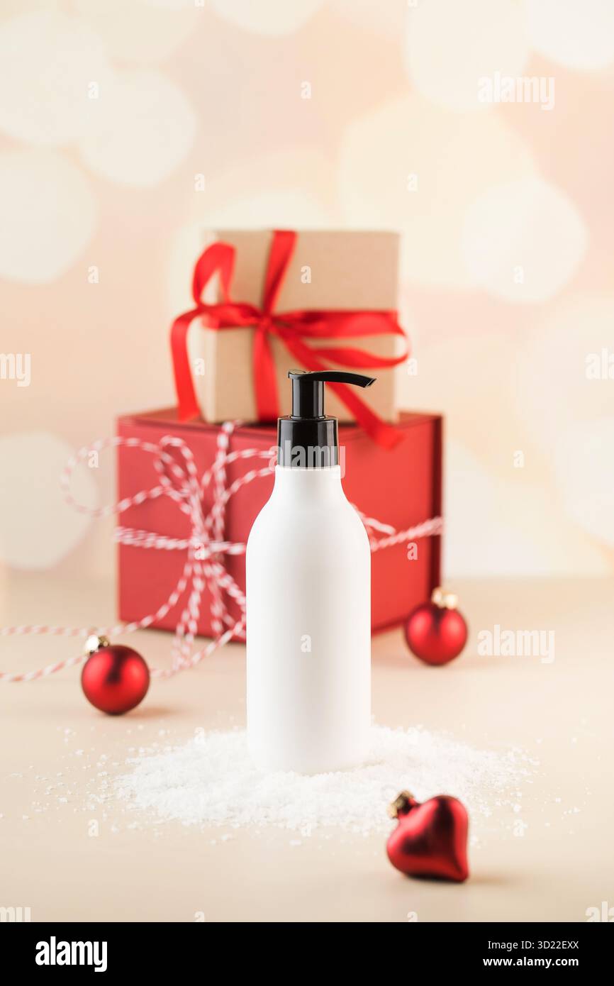 Maquette d'un distributeur blanc avec un produit cosmétique sur la neige sur fond de cadeaux de Noël. Banque D'Images