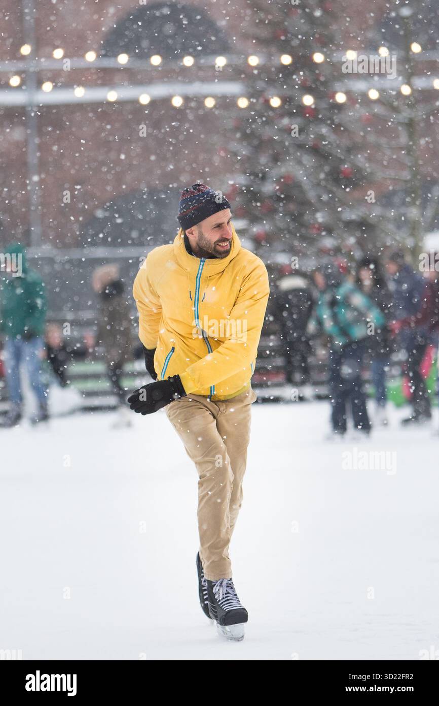 Joyeux homme d'âge moyen en veste jaune, pantalon beige sur la patinoire, à l'extérieur dans la journée d'hiver enneigée Banque D'Images