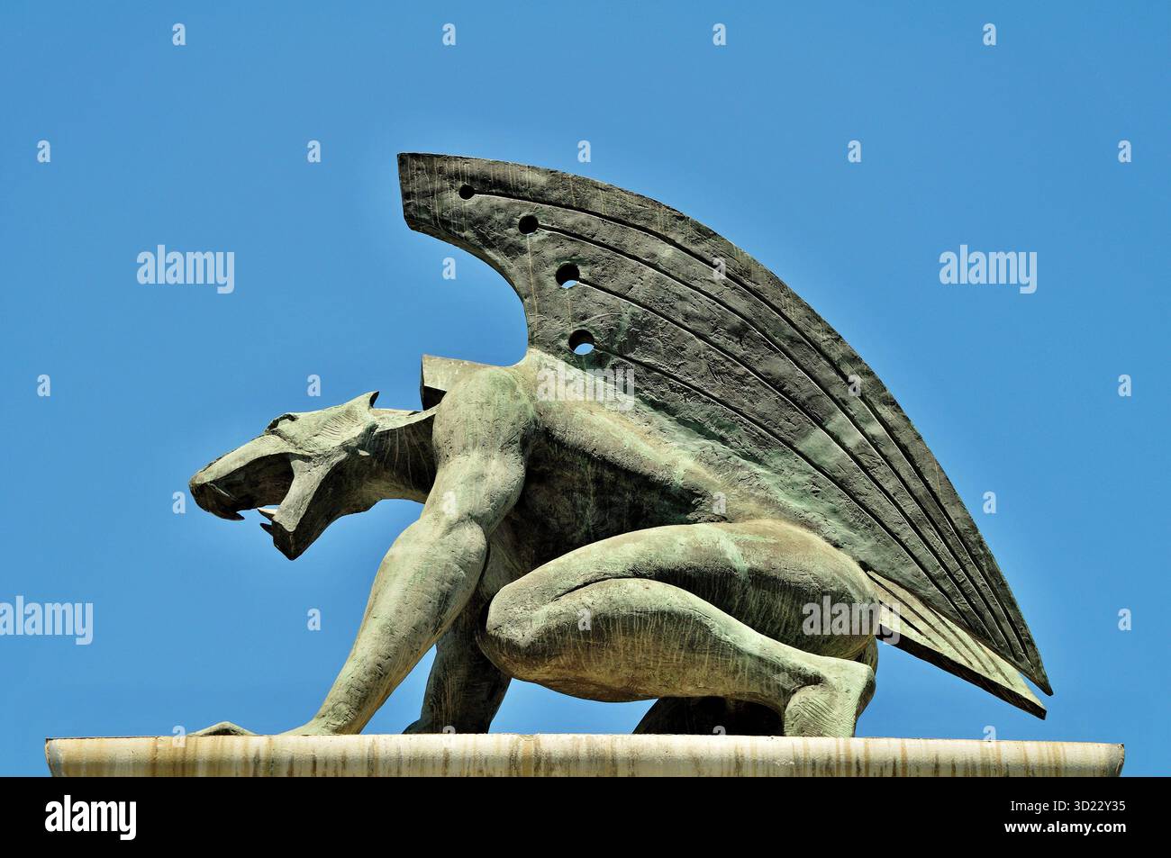 Statue de créature mythique avec des ailes et des dents acérées gardant un bâtiment sous un ciel bleu clair Banque D'Images