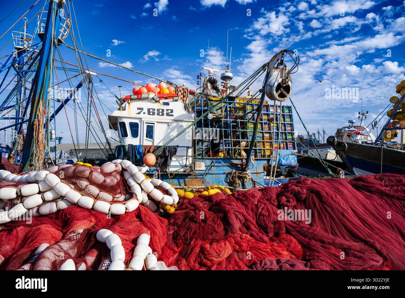 Un bateau de pêche coloré amarré à un port, entouré de filets rouges et blancs vibrants. Essaouira, Maroc Banque D'Images