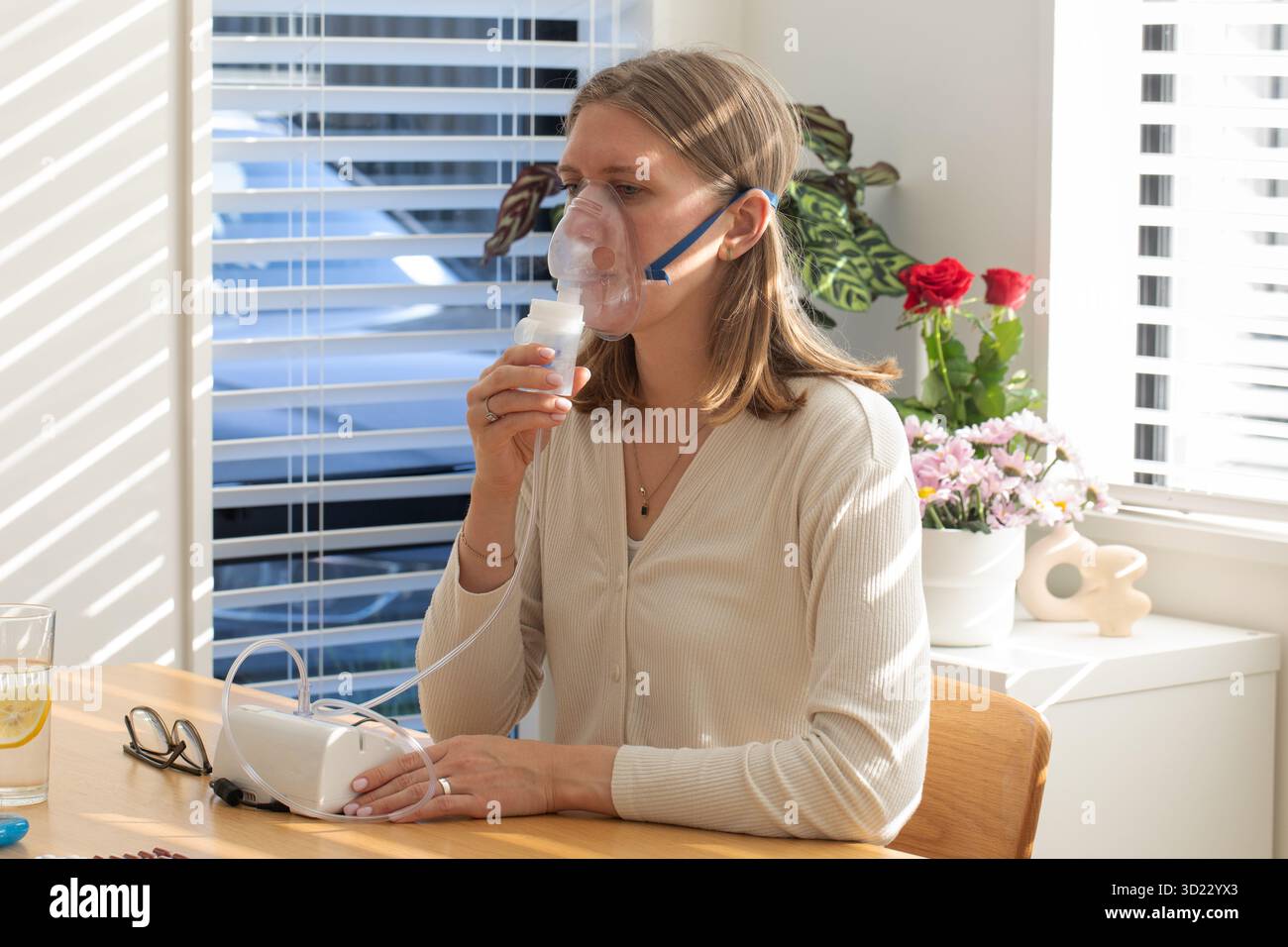 Femme utilisant un nébuliseur pour la santé respiratoire dans un cadre lumineux à la maison. Concept de santé Banque D'Images