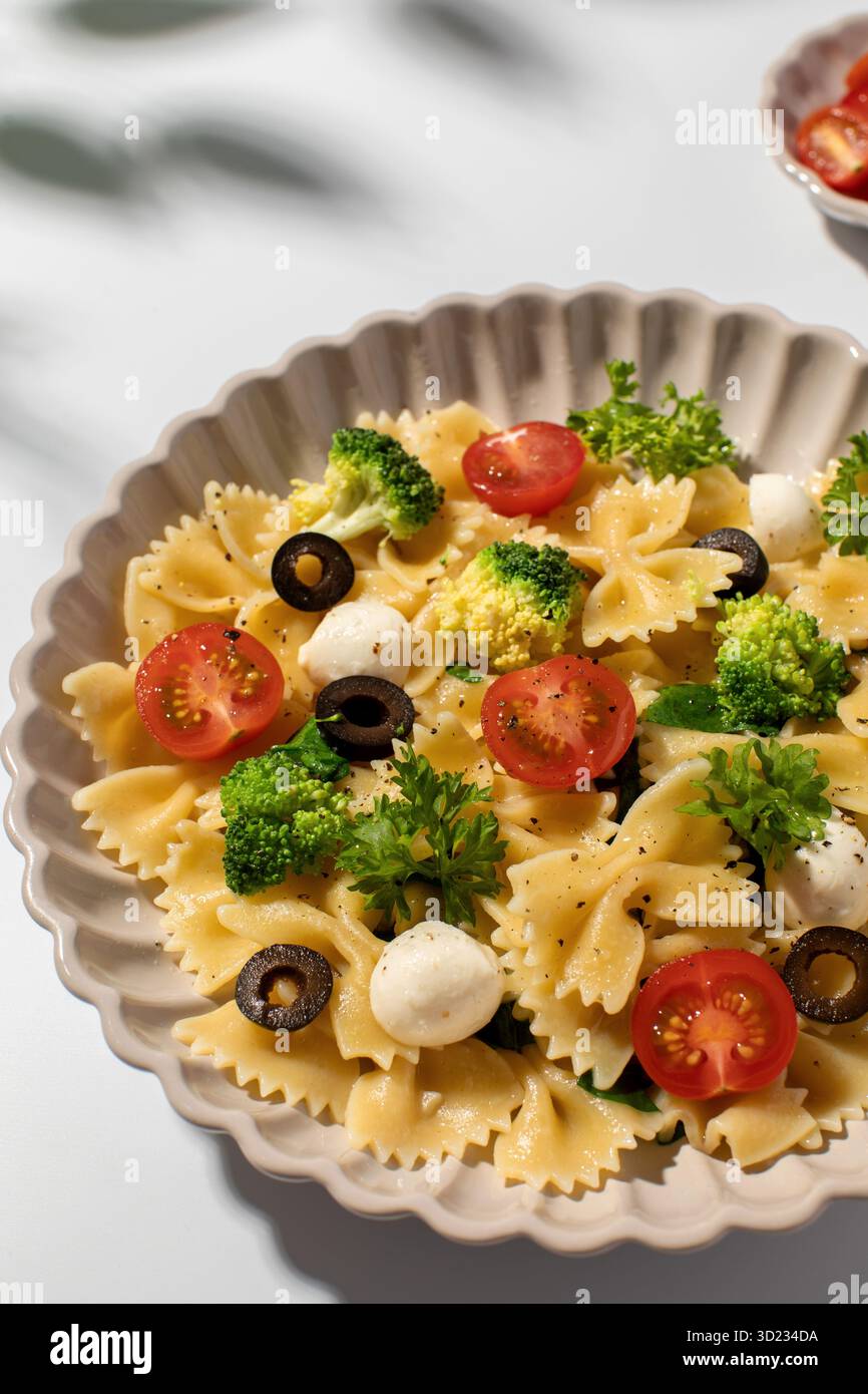 Salade de pâtes colorées avec farfalle, tomates cerises, olives, mozzarella, brocoli, et persil sur fond blanc Banque D'Images