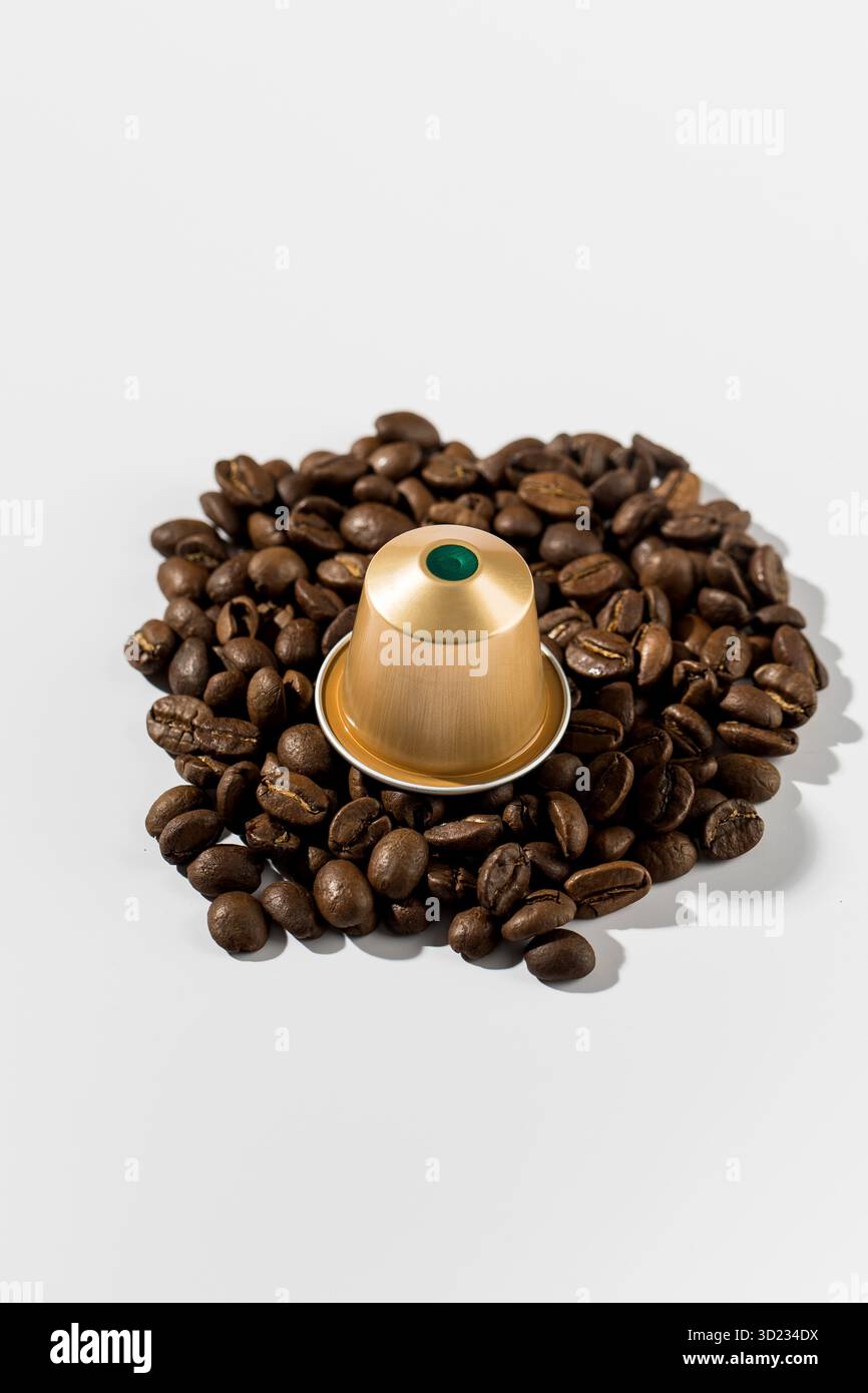 Capsule de café doré sur grains de café sur un fond blanc. Publicité Banque D'Images