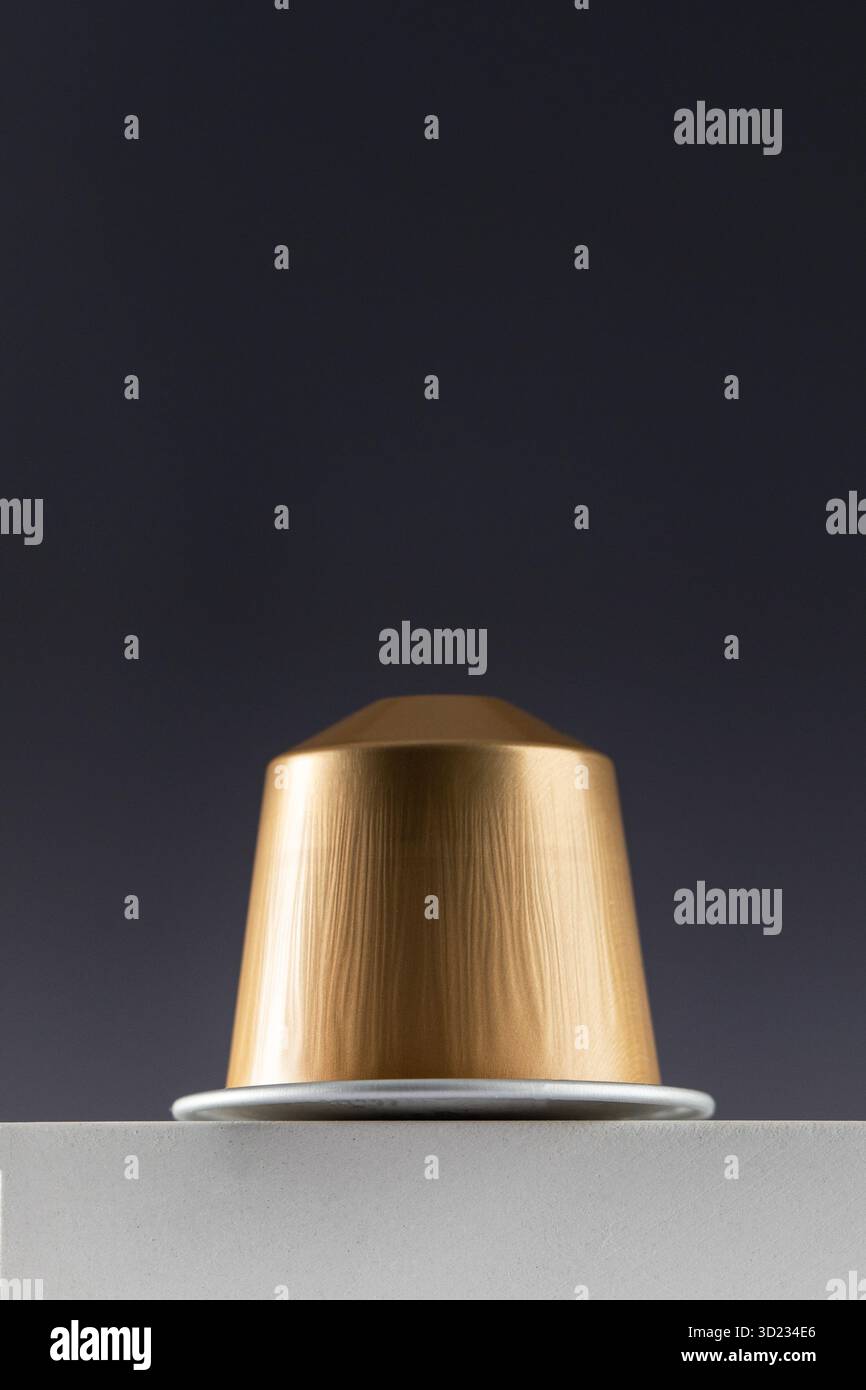 Capsule de café doré sur un bloc blanc sur un fond dégradé foncé Banque D'Images