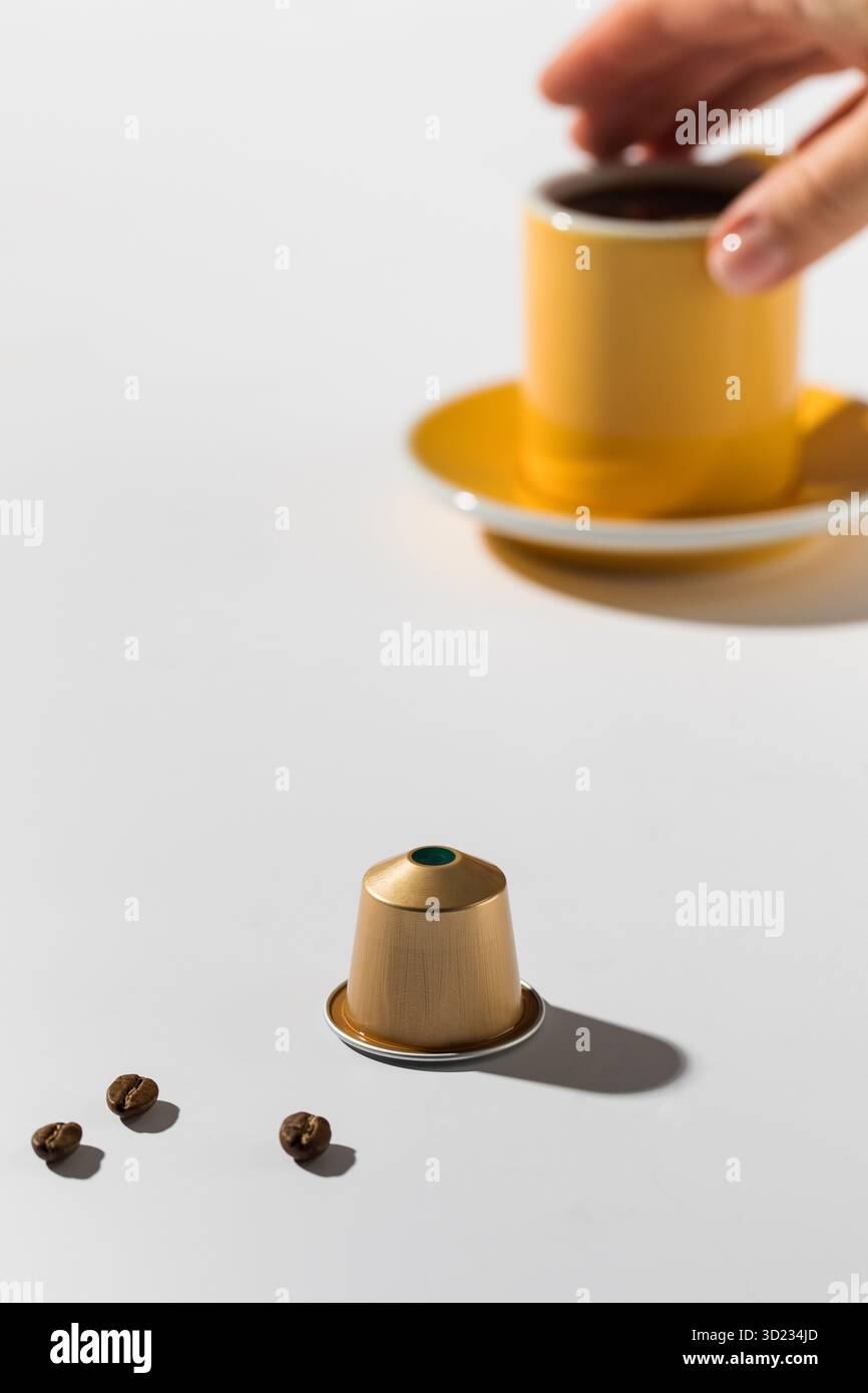 Capsule de café doré et une tasse de café sur un fond blanc Banque D'Images