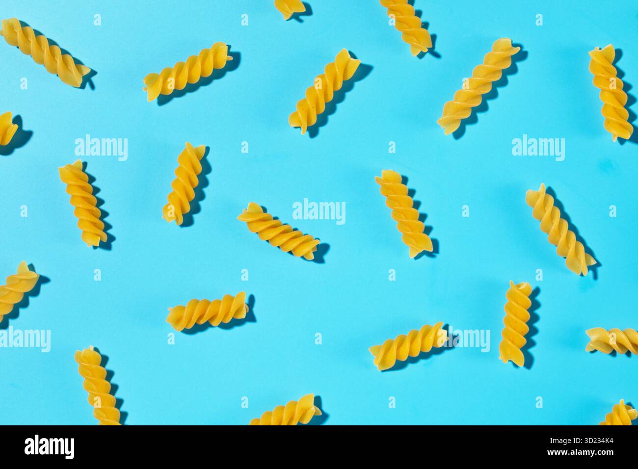 Spirales de pâtes fusilli non cuites dispersées sur un fond bleu dans un motif décoratif Banque D'Images
