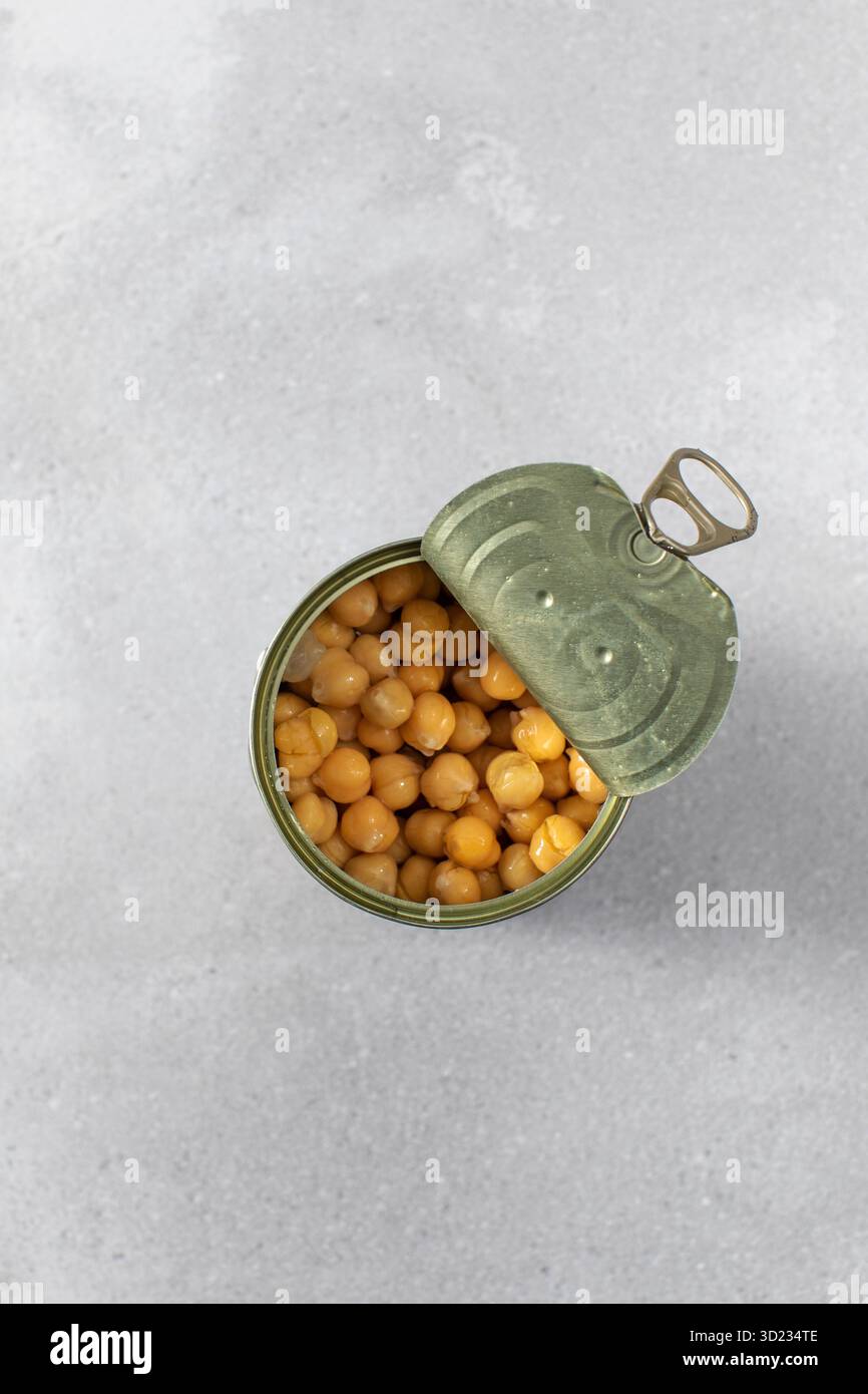 Boîte de conserve ouverte avec de savoureux pois chiches conservés sur gris clair Banque D'Images