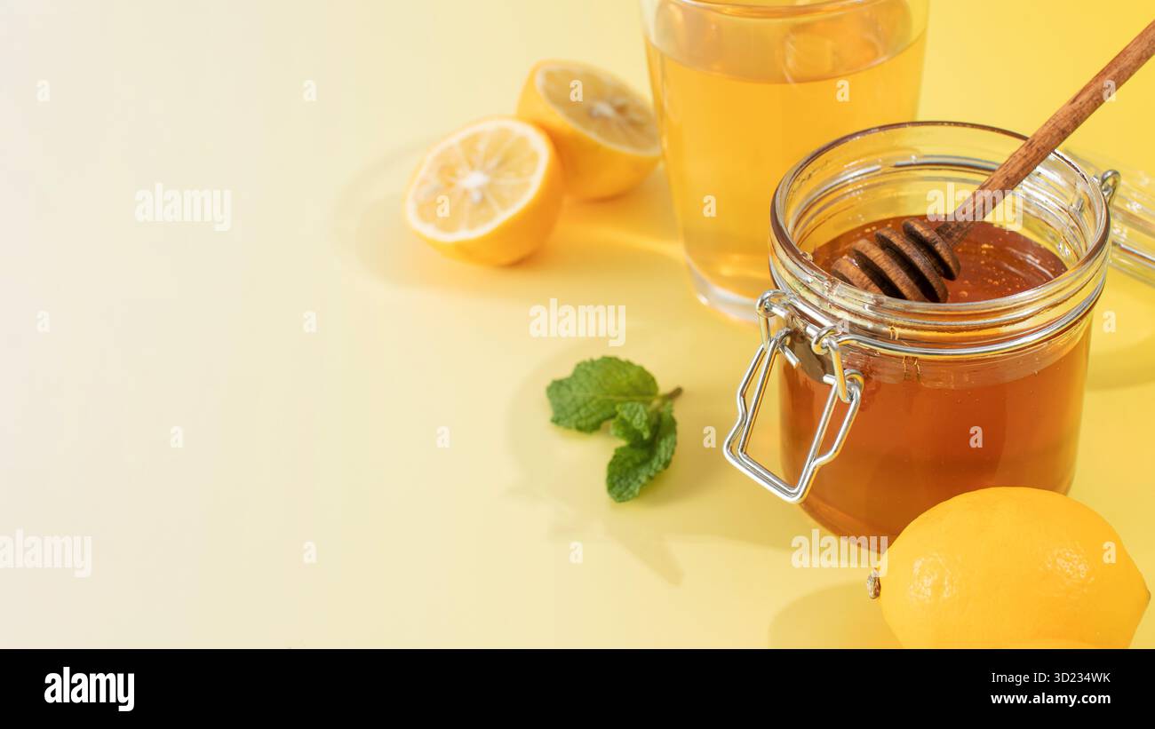 Un pot de miel avec une louche de miel avec des feuilles de menthe et des tranches de citron. Banque D'Images