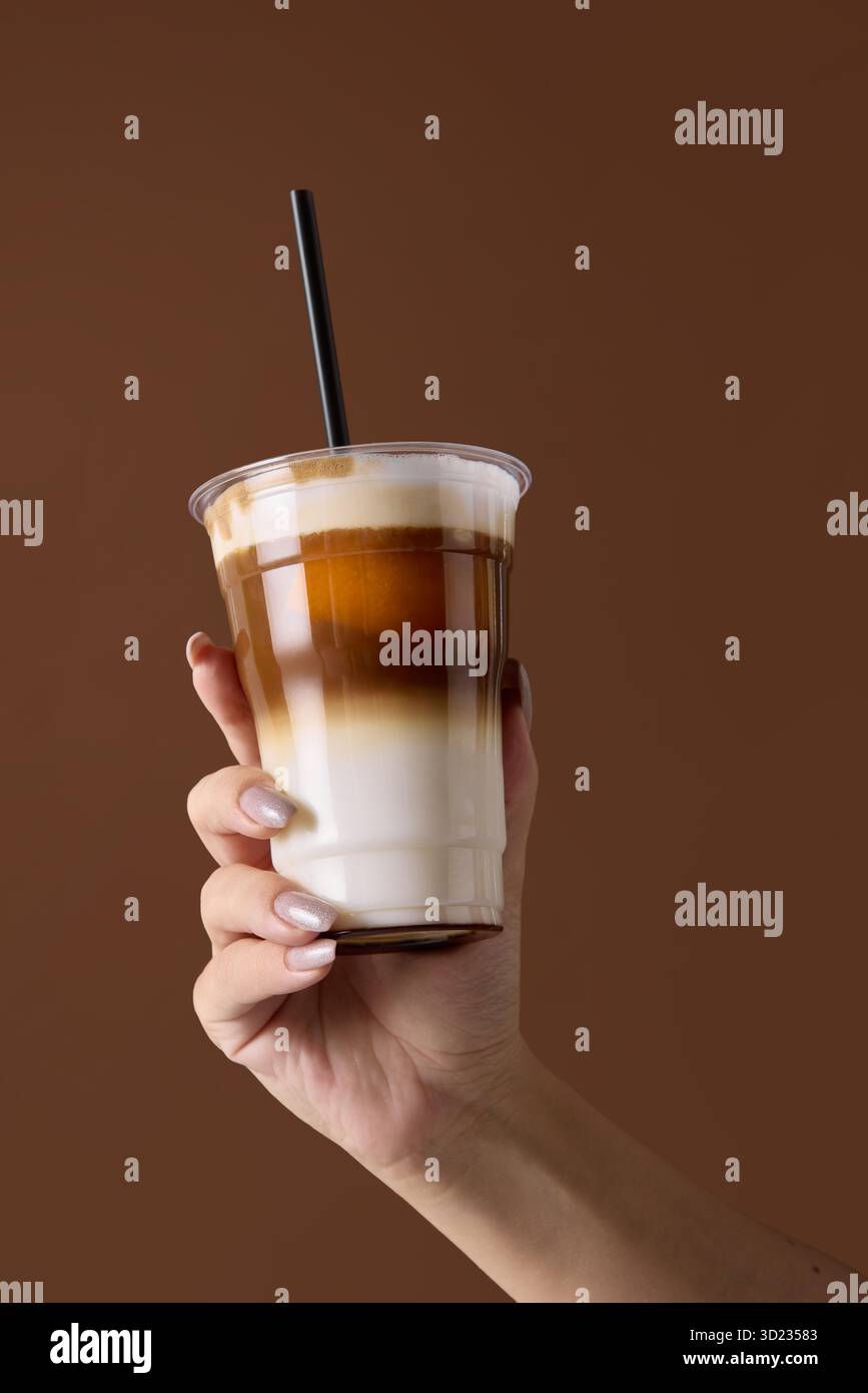 Main tenant le latte glacé dans un gobelet en plastique avec paille sur fond brun pour le marquage de la boisson Banque D'Images