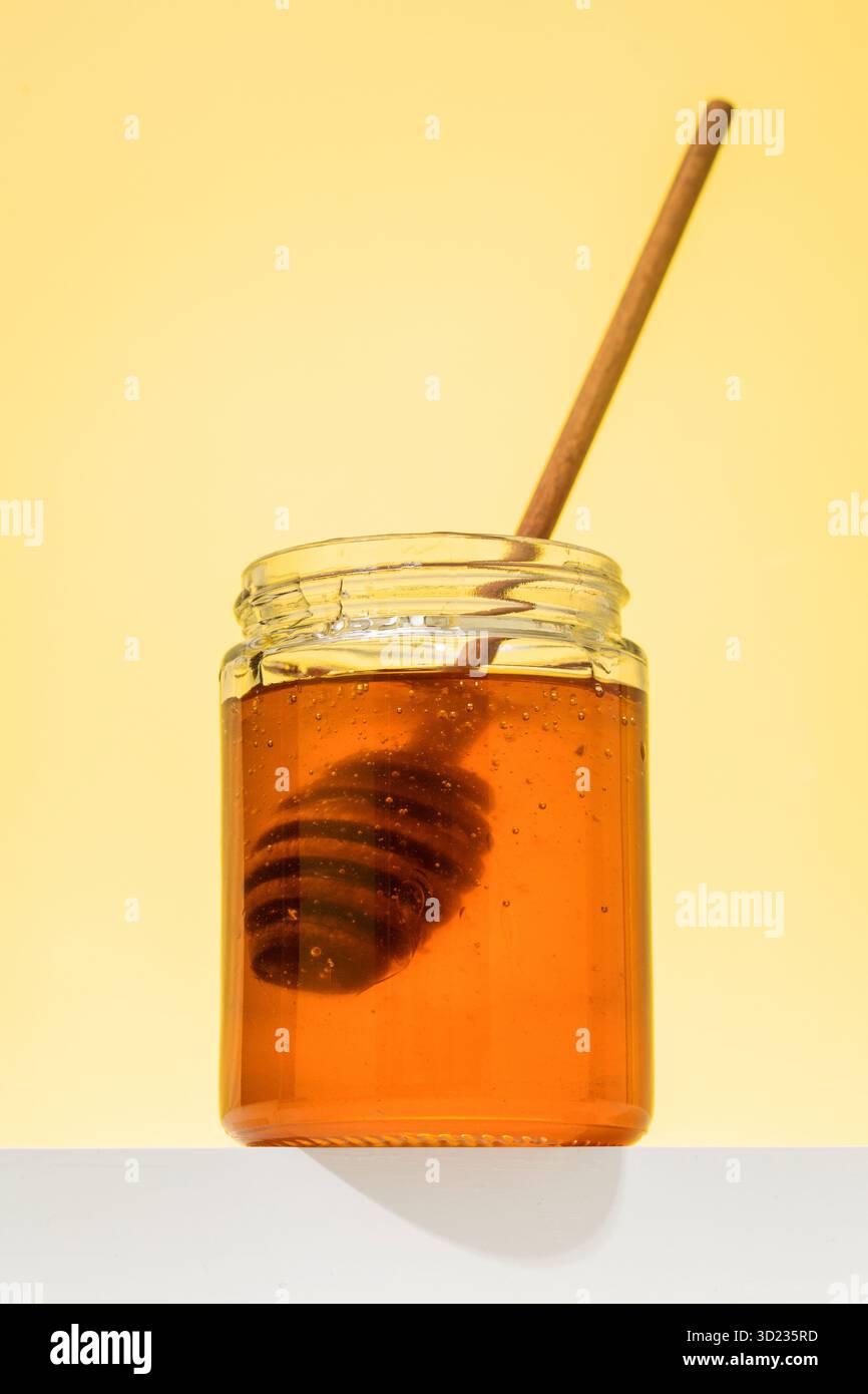 Miel floral doré dans un pot avec une louche en bois sur le podium. Organique et sain. Banque D'Images