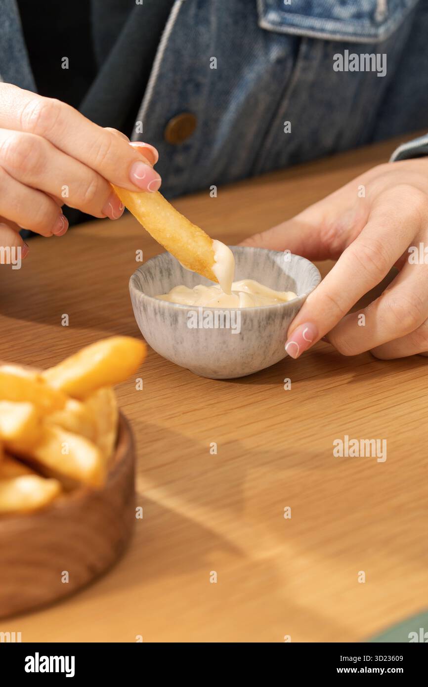 La femme déverse des frites dans la sauce à la table en bois Banque D'Images