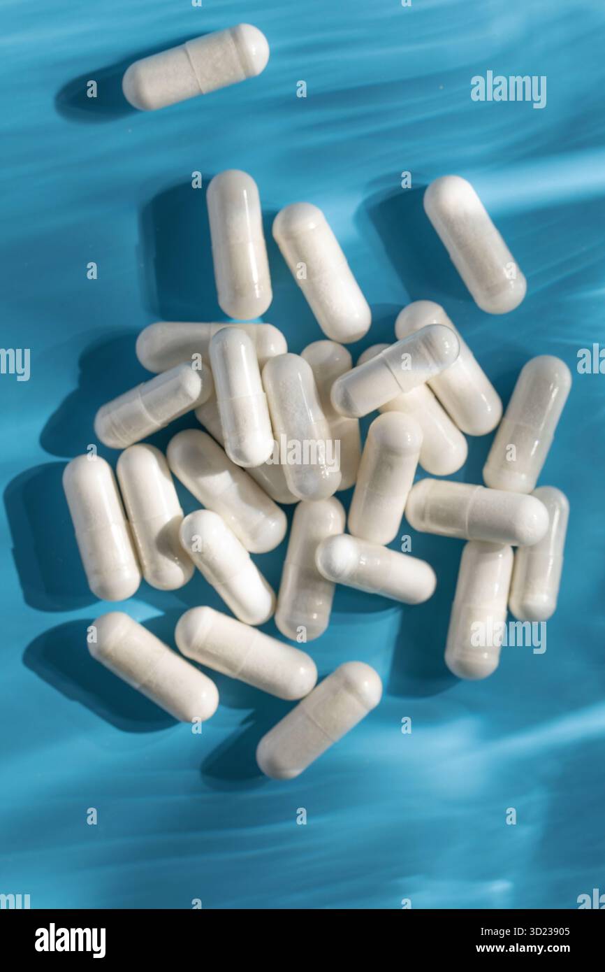 Capsules médicinales blanches, vitamines ou compléments alimentaires en gros plan sur fond bleu. Médecine Banque D'Images