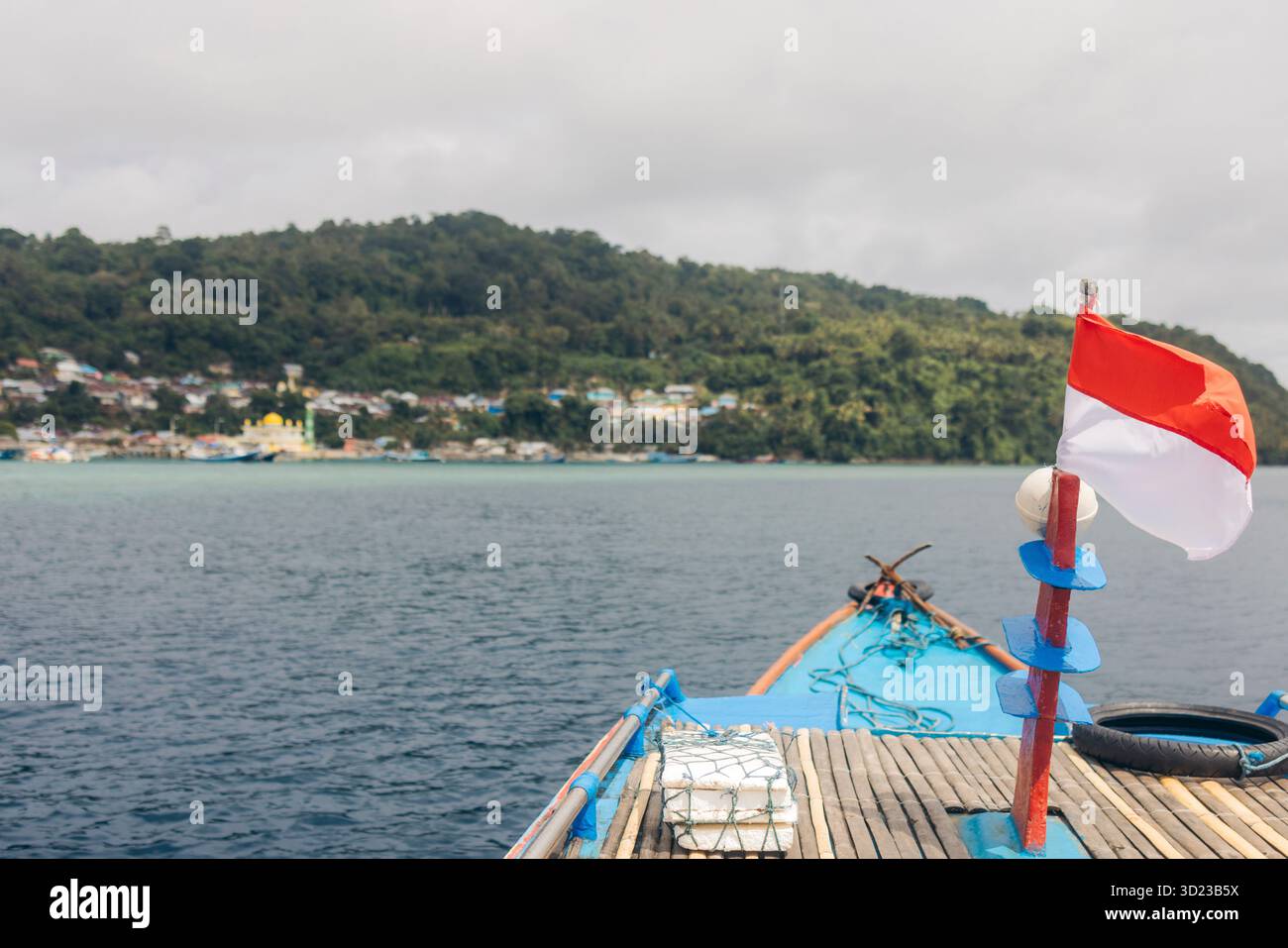 Bateau en bois sur l'eau calme avec le drapeau indonésien et collines boisées en arrière-plan. Pulau Rhun ou Rhun Island, Banda, Central Maluku Regency, Indonésie Banque D'Images