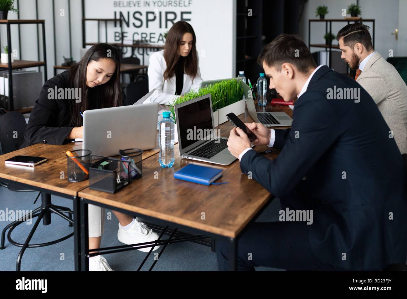 Jours ouvrables dans le bureau les employés assis dans un espace ouvert et travaillent sur des ordinateurs portables et des téléphones dans des vêtements d'affaires multinationaux collégial Banque D'Images