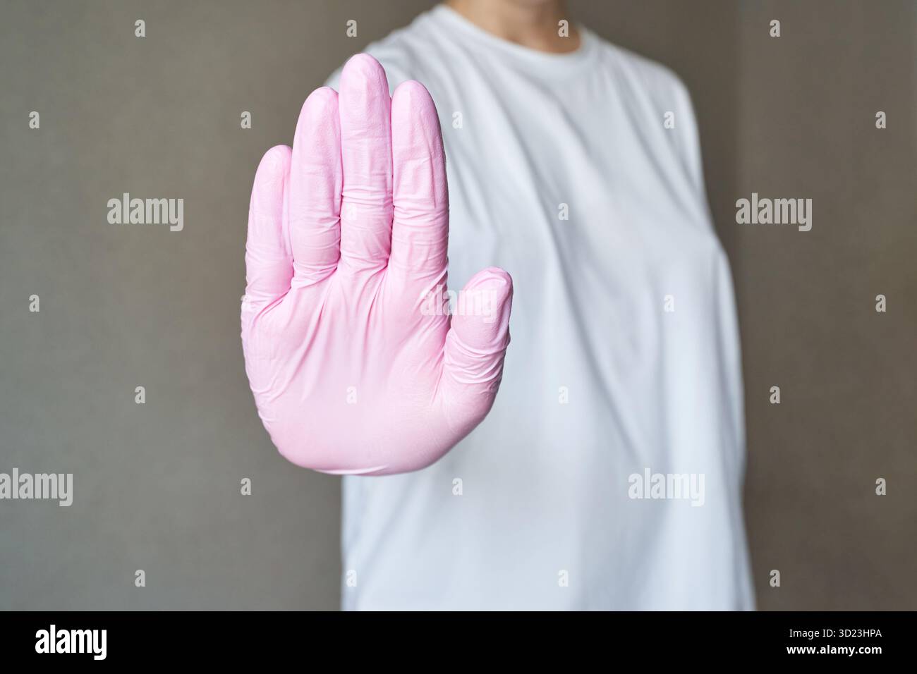 Femme adulte caucasienne portant un gant rose faisant un geste stop contre le gris Banque D'Images