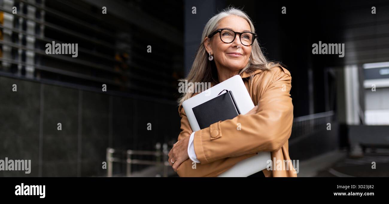 Portrait d'une femme d'affaires âgée avec un ordinateur portable dans des lunettes à l'extérieur du bureau, concept de femme forte et indépendante Banque D'Images