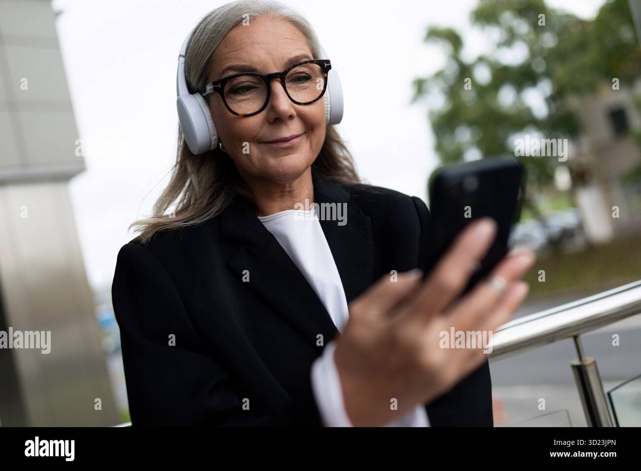 Femme âgée élégante écoutant de la musique dans des écouteurs avec un téléphone dans ses mains Banque D'Images