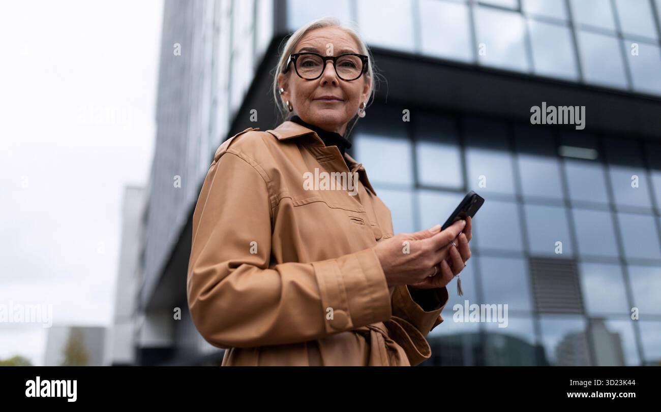 Portrait d'une femme d'affaires mature réussie avec un téléphone portable dans ses mains sur fond d'une façade en verre d'un offi Banque D'Images