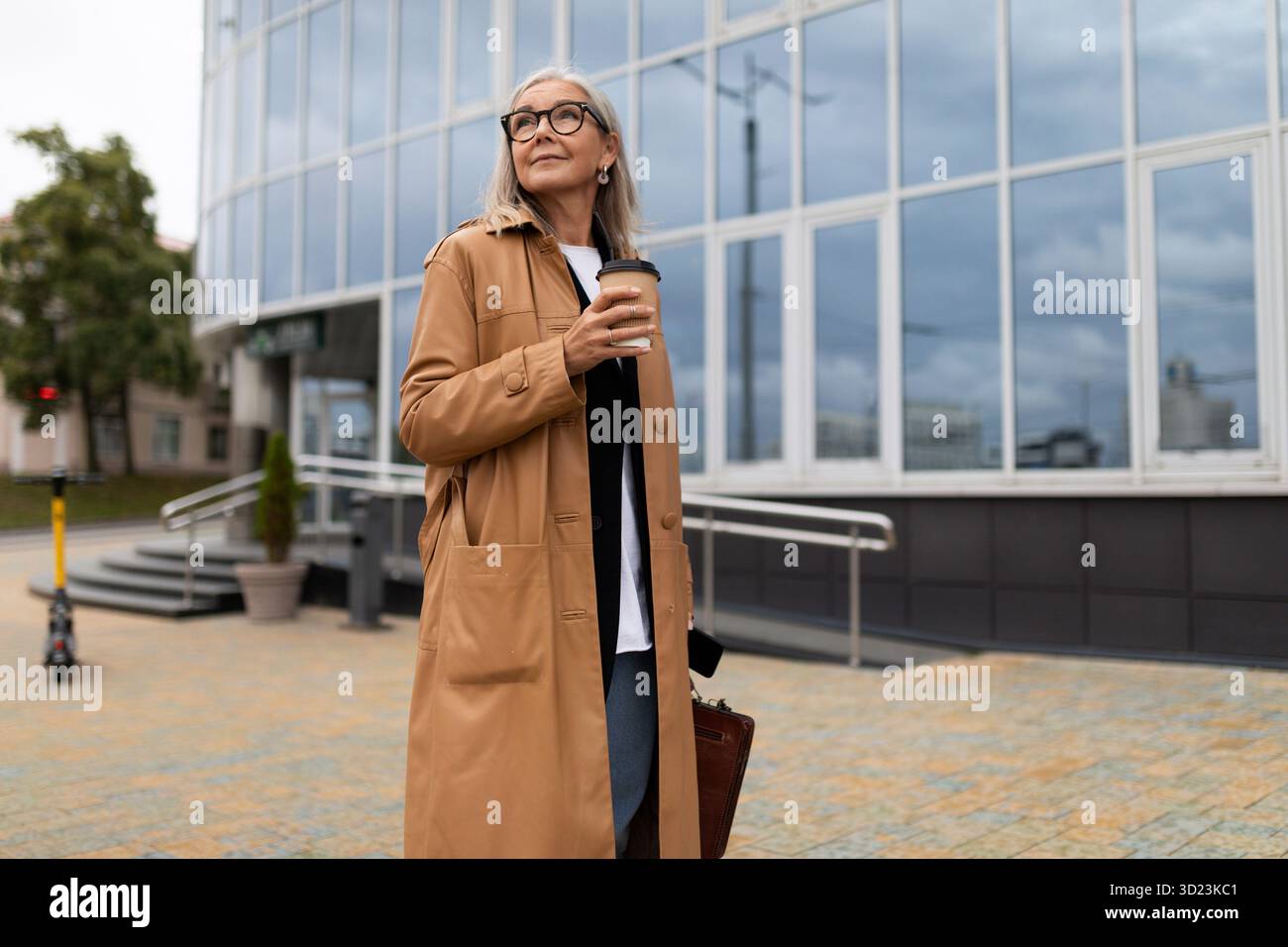 Femme d'affaires élégante tête de stands de 50 ans avec un verre de café sur le fond du centre de bureau Banque D'Images