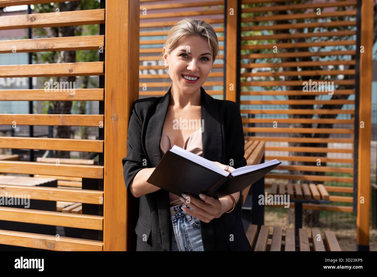 Portrait en demi-longueur d'une femme d'affaires prospère avec un journal d'affaires à côté d'un mur en bois dans la rue Banque D'Images
