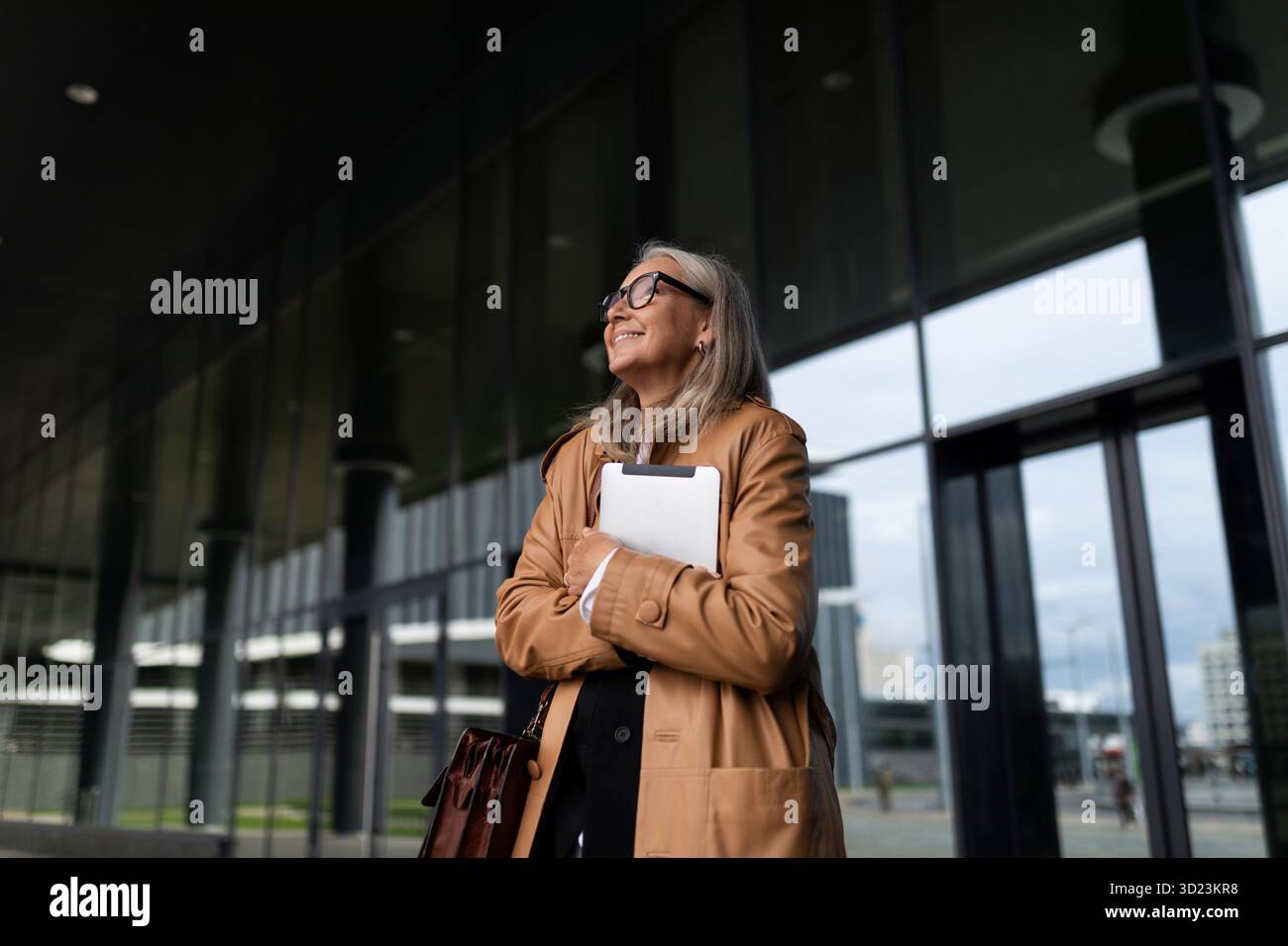Une femme d'affaires de cinquante ans en âge de retraite quitte l'immeuble de bureaux regarde autour de lui avec un ordinateur portable dans ses mains Banque D'Images
