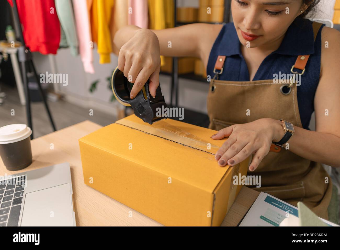 Jeune femme entrepreneure scellant soigneusement le paquet avec du ruban adhésif, préparant les commandes de marchandises, gérant l'expédition et la livraison pour son succès en ligne Banque D'Images
