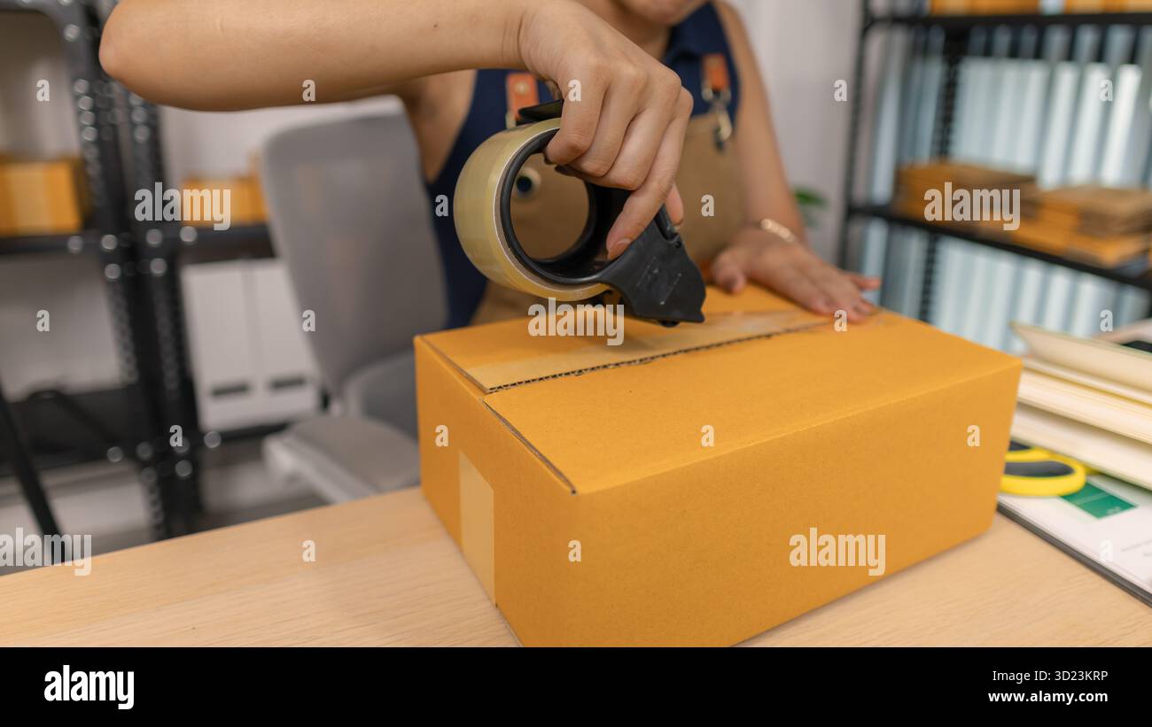 Jeune femme entrepreneure scellant soigneusement le paquet avec du ruban adhésif, préparant les commandes de marchandises, gérant l'expédition et la livraison pour son succès en ligne Banque D'Images