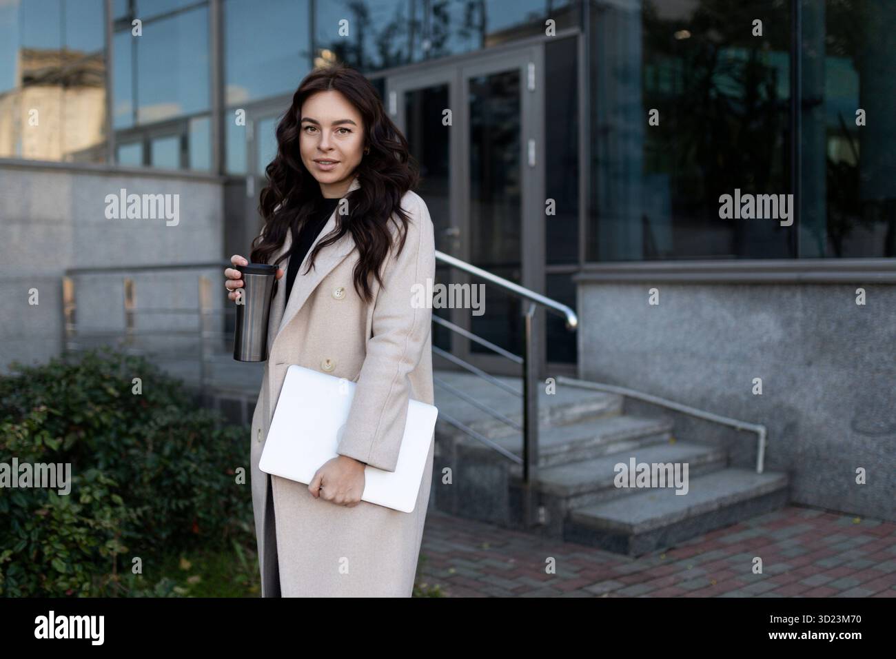 Femme indépendante moderne avec un ordinateur portable dans ses mains dans le contexte d'un immeuble de bureaux, dirigeant une entreprise prospère Co Banque D'Images