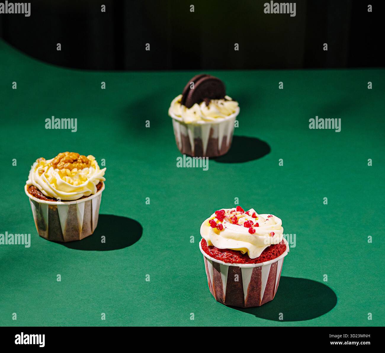 Cupcakes colorés disposés sur une surface verte lors d'un éclairage vif Banque D'Images