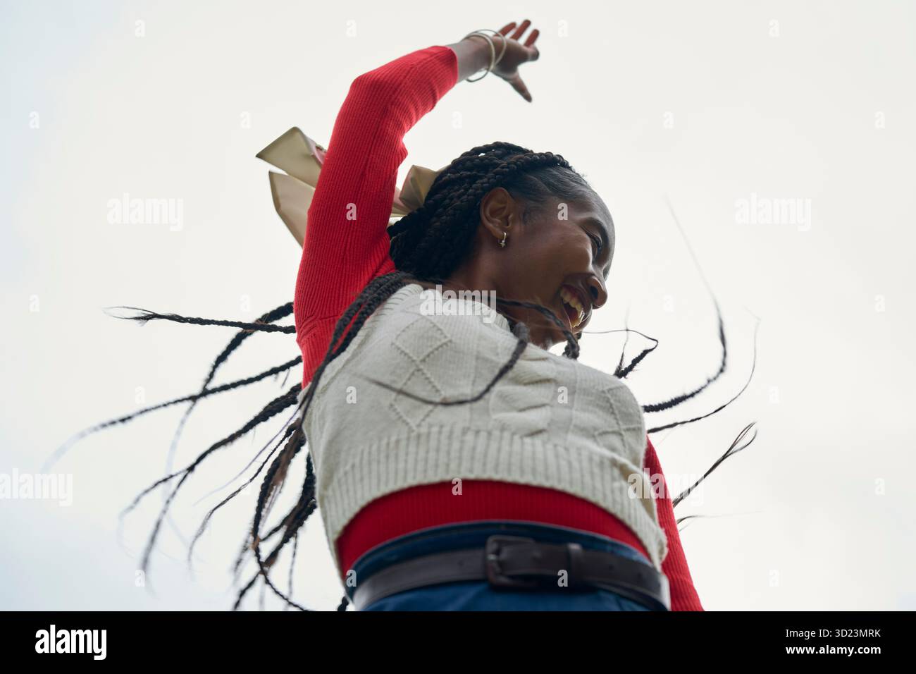 Femme souriante avec des cheveux tressés et un pull rouge sur un fond de ciel clair. Bruges, Belgique Banque D'Images