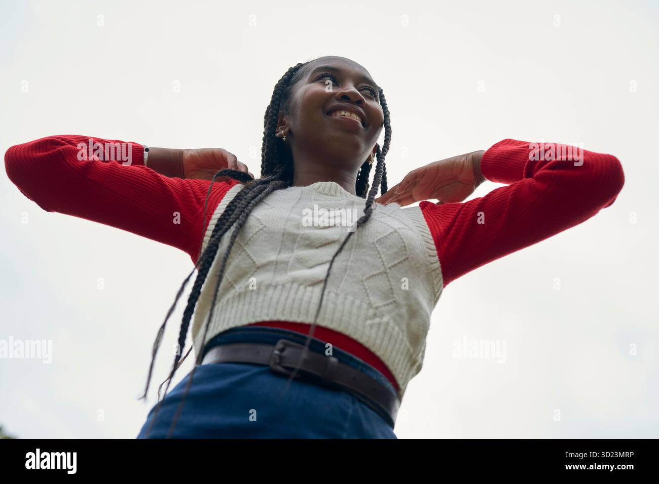 Femme souriante avec des cheveux tressés et un pull rouge sur un fond de ciel clair. Bruges, Belgique Banque D'Images