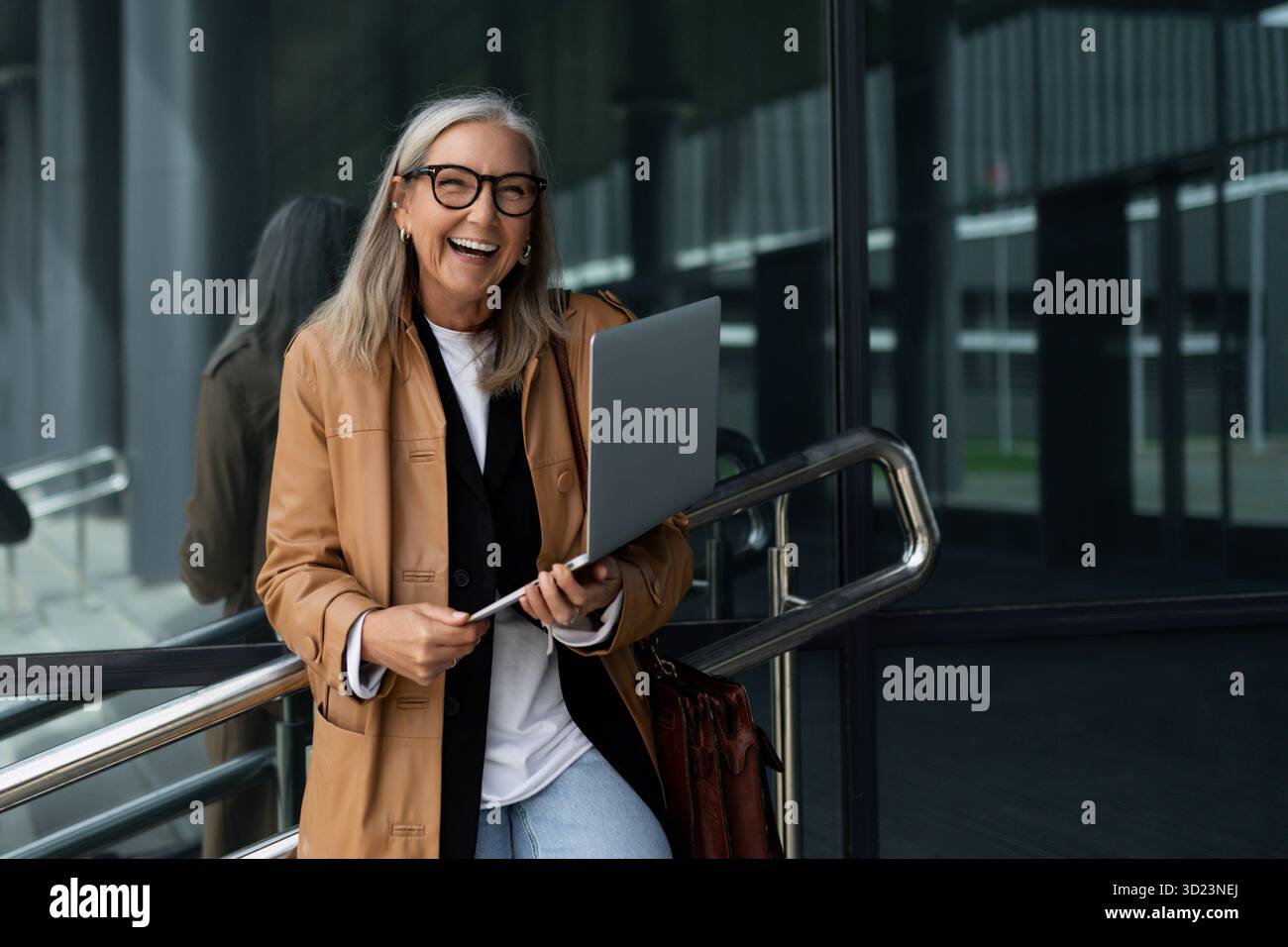 Femme d'affaires de cinquante ans avec un ordinateur portable dans les mains sourit largement en dehors du bureau Banque D'Images