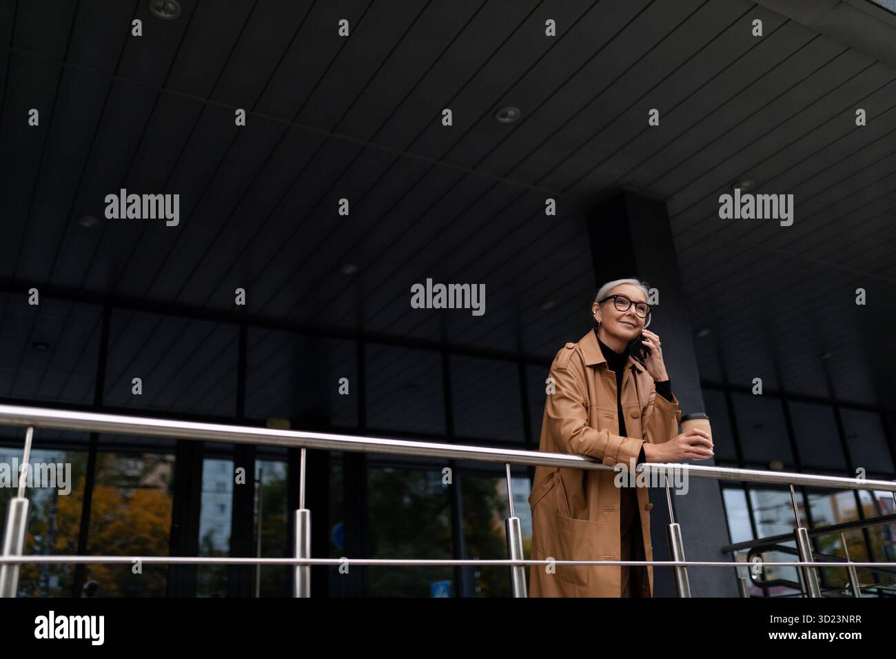 Femme âgée élégante parlant sur le téléphone portable près de l'immeuble de bureaux Banque D'Images
