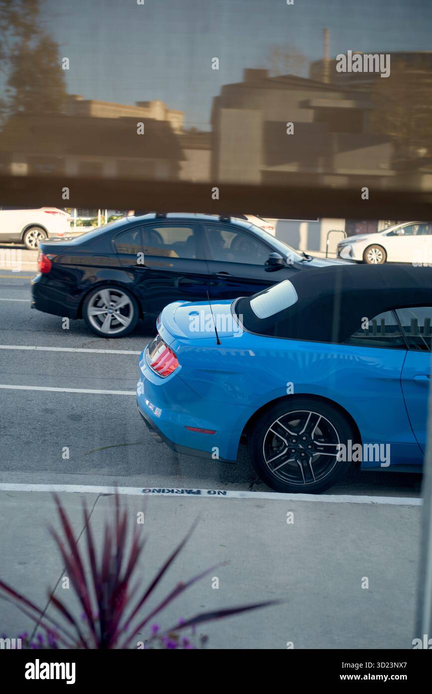 Deux voitures garées dans une rue de la ville vues à travers une fenêtre avec des stores. Californie, États-Unis Banque D'Images