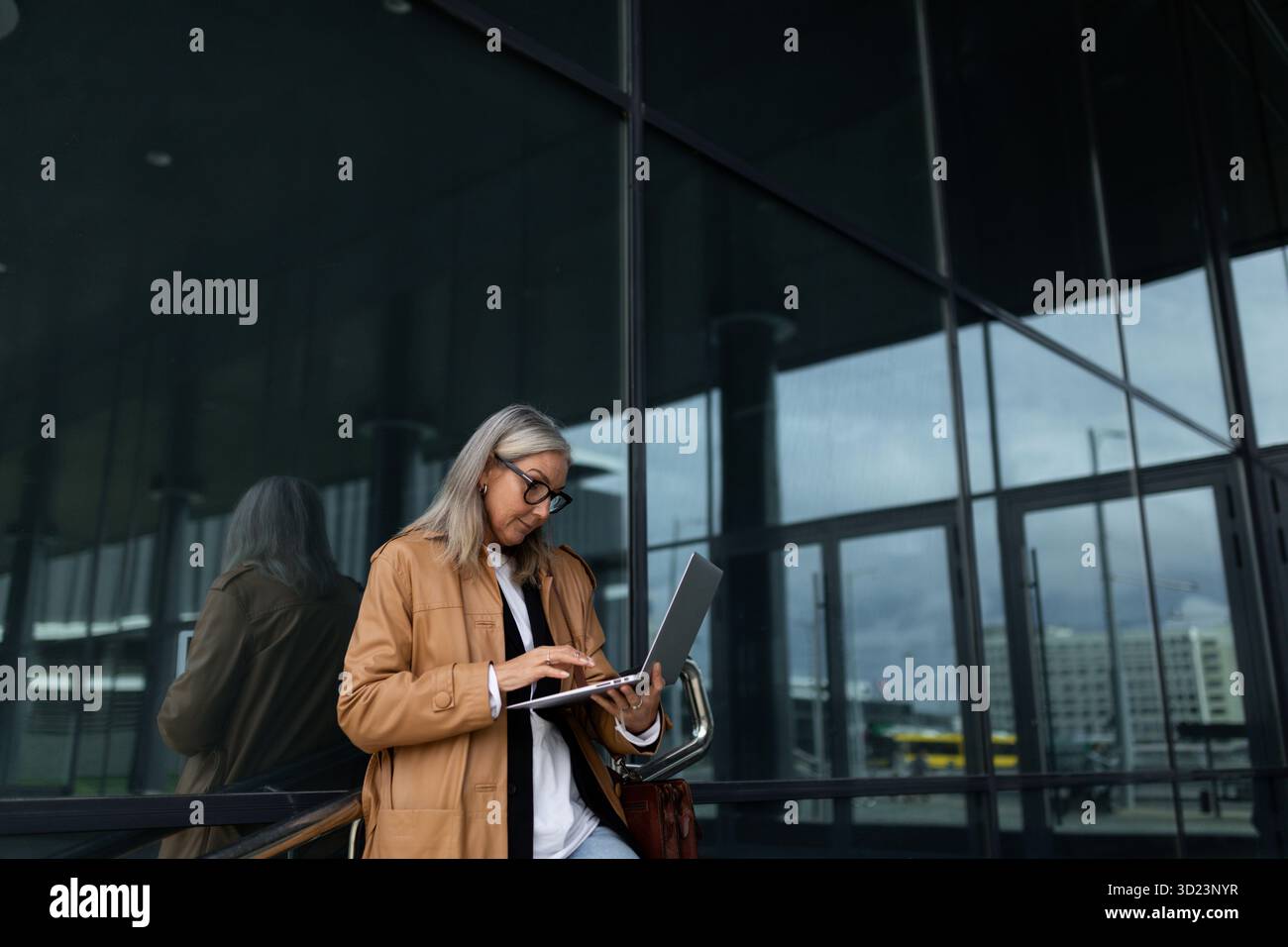 Élégante femme de cinquante ans travaillant sur un ordinateur portable à l'entrée de l'immeuble de bureaux Banque D'Images
