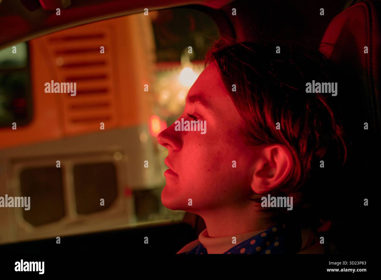 Jeune femme en vue de profil à l'intérieur d'une voiture la nuit, éclairée par la lumière rouge. Californie, États-Unis Banque D'Images