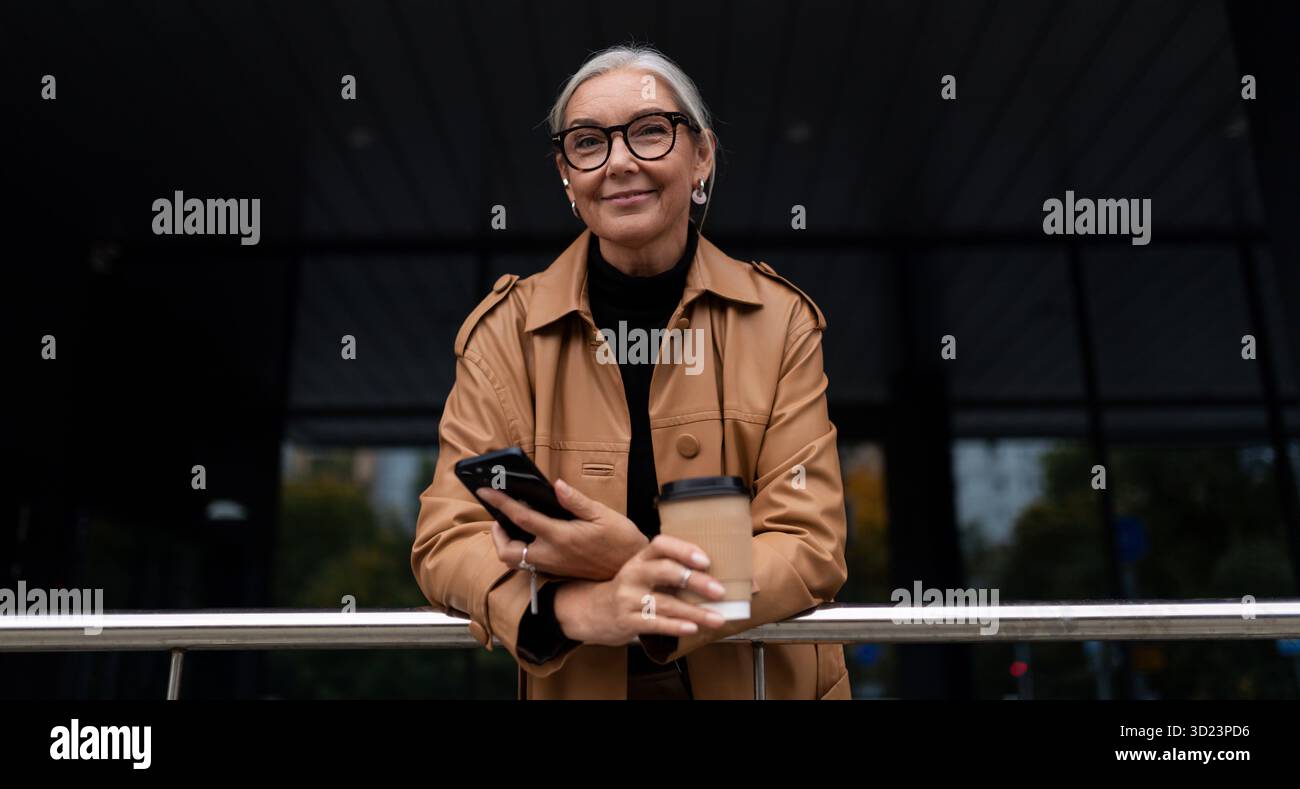 Portrait d'une femme d'affaires élégante de cinquante ans avec un téléphone et une tasse de café dans ses mains Banque D'Images