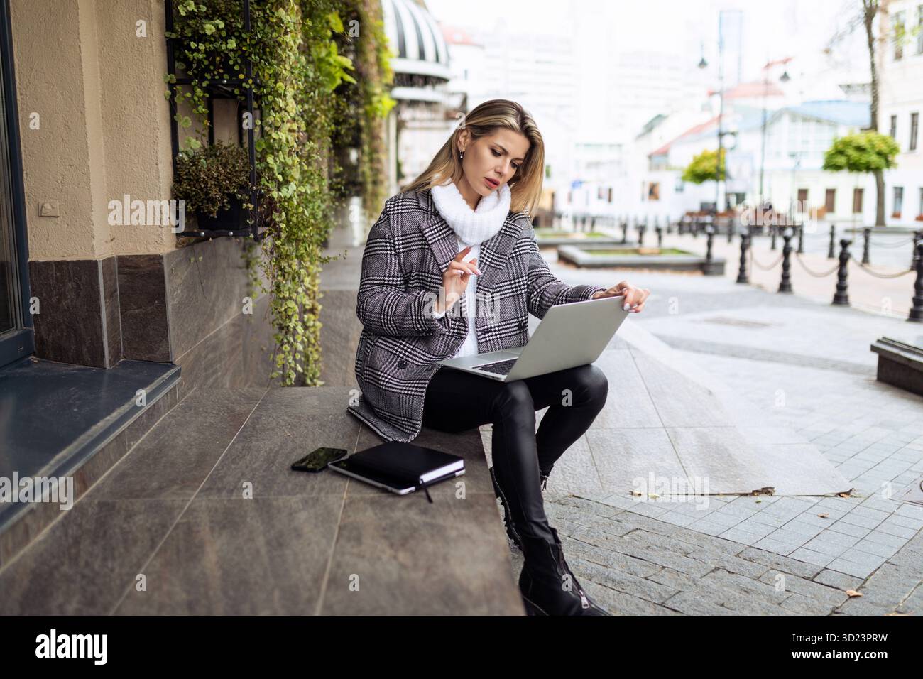 Femme d'affaires mature travaillant sur un ordinateur portable en ligne assis sur les marches à l'entrée de l'immeuble de bureaux sur le fond de Banque D'Images