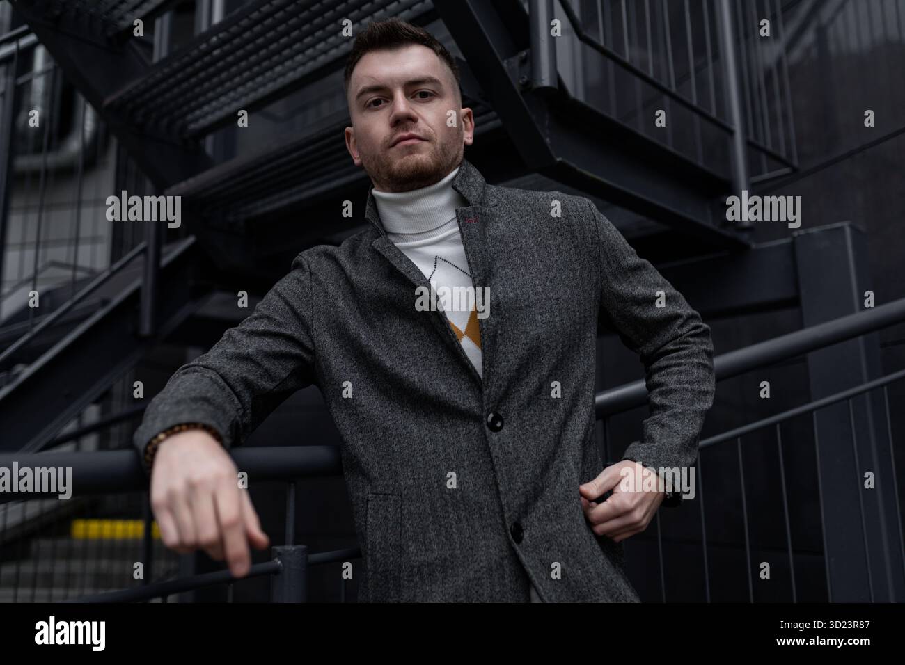Portrait élégant d'un homme brutal dans un manteau sur le fond d'un bâtiment noir Banque D'Images