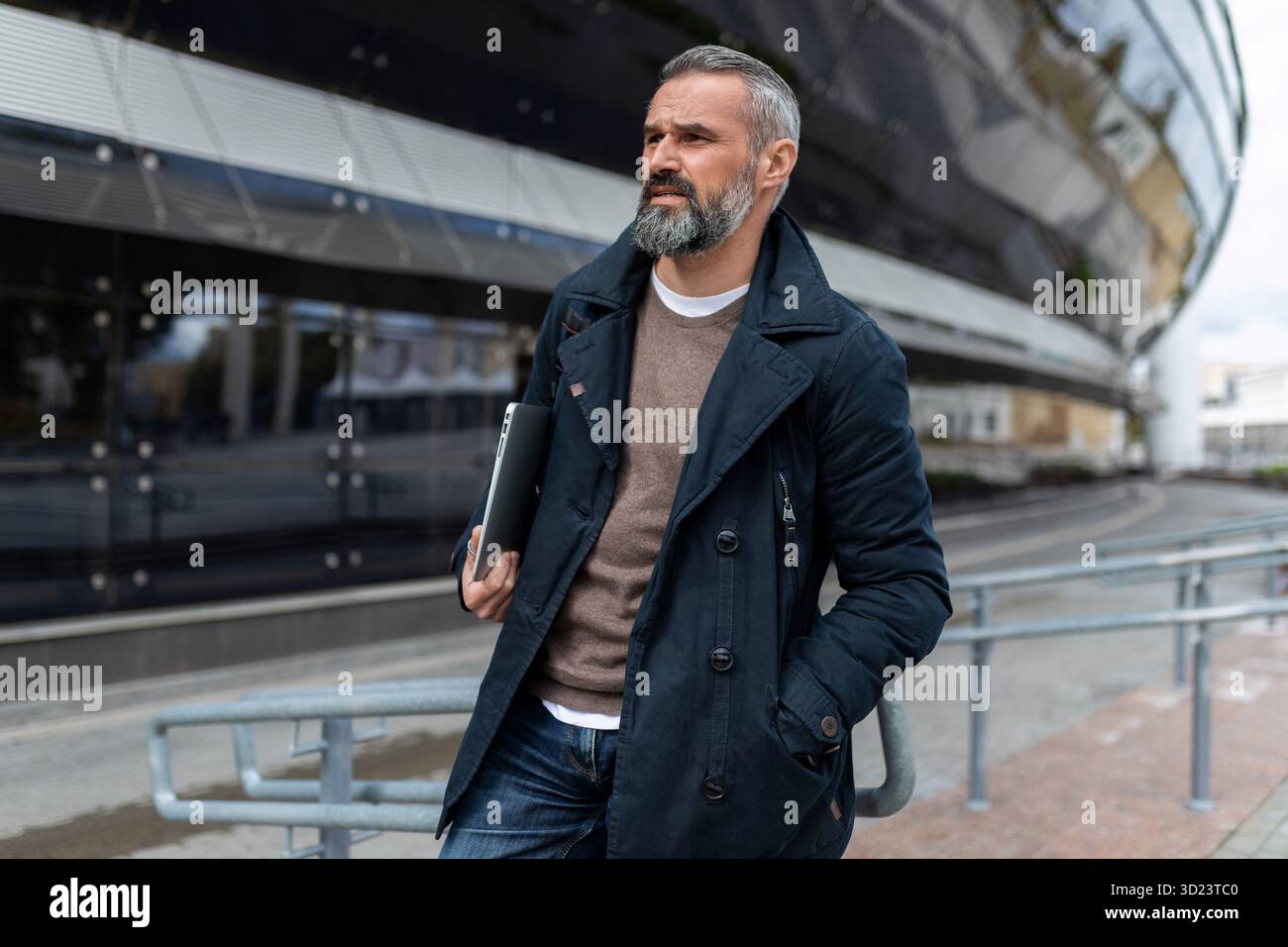 Portrait d'un homme d'affaires de 50 ans avec un ordinateur portable marchant le long de l'immeuble de bureaux Banque D'Images